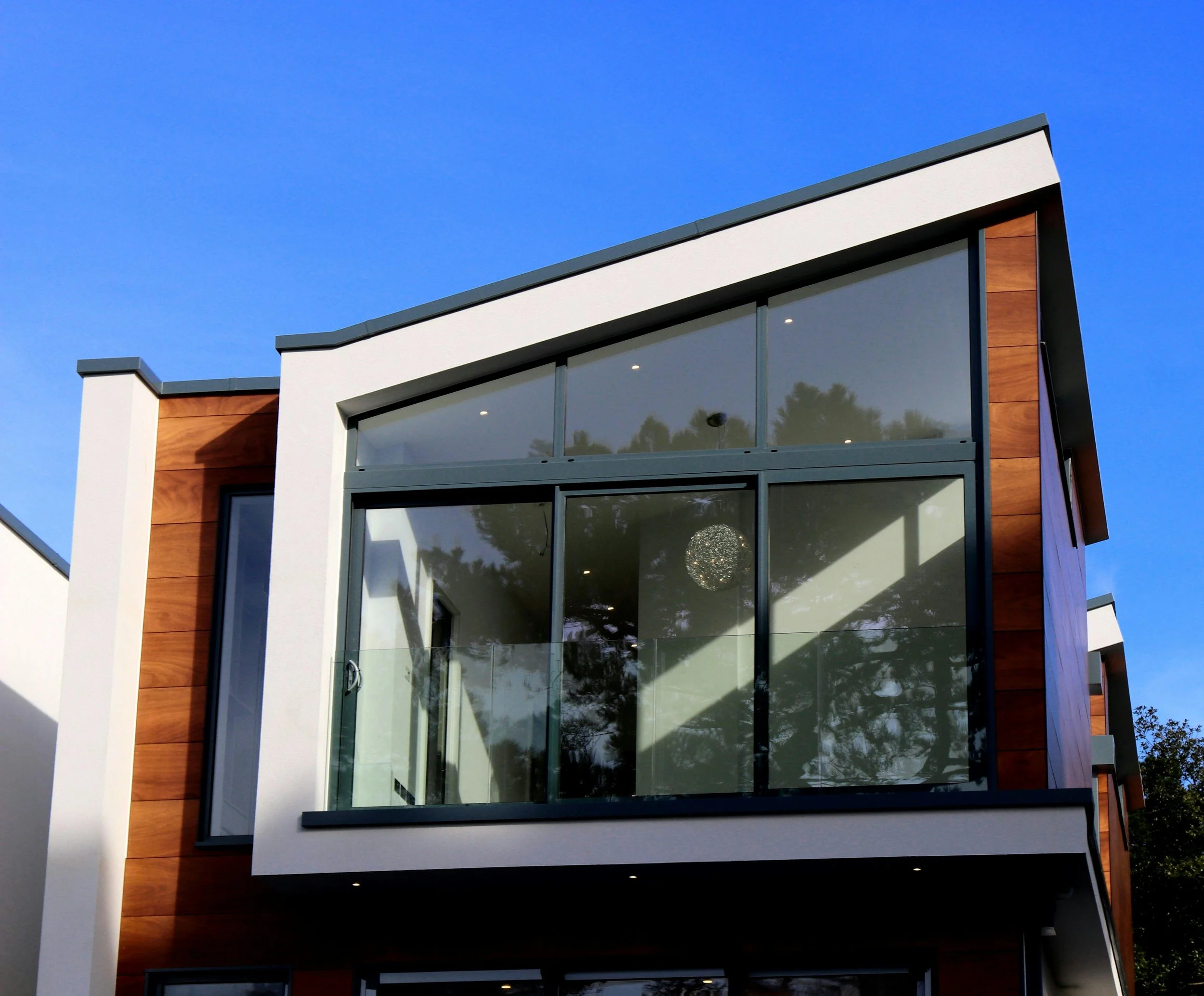 Modern house with large glass windows, wooden panel accents, and a sloped roof under a clear blue sky.