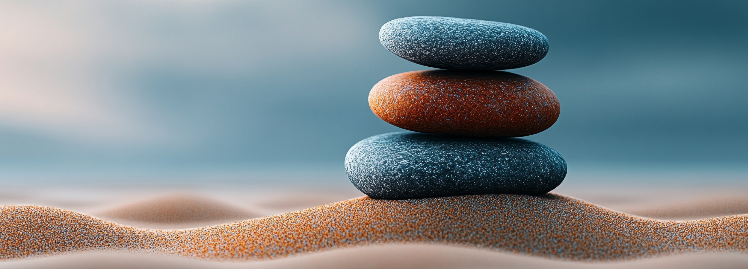 Four smooth, flat stones balanced on top of each other on sandy terrain, with a blurred background.