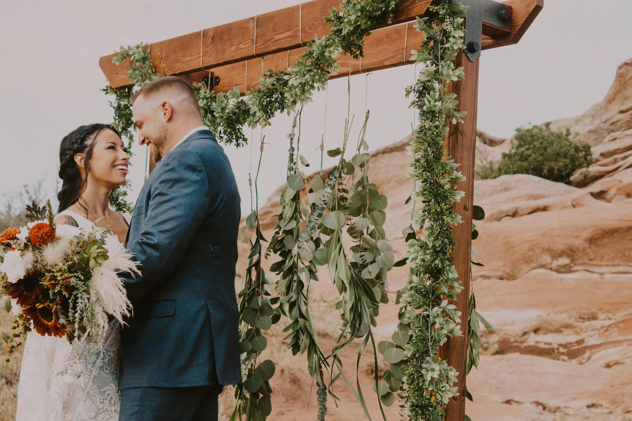  Posed beneath their wedding arch, Denver, Colorado photographer, Dawn Louise Photography captures bohemian bride and groom celebrating after their Colorado Red Rocks wedding ceremony. stained wood wedding arch, garland wedding arch installment, garl