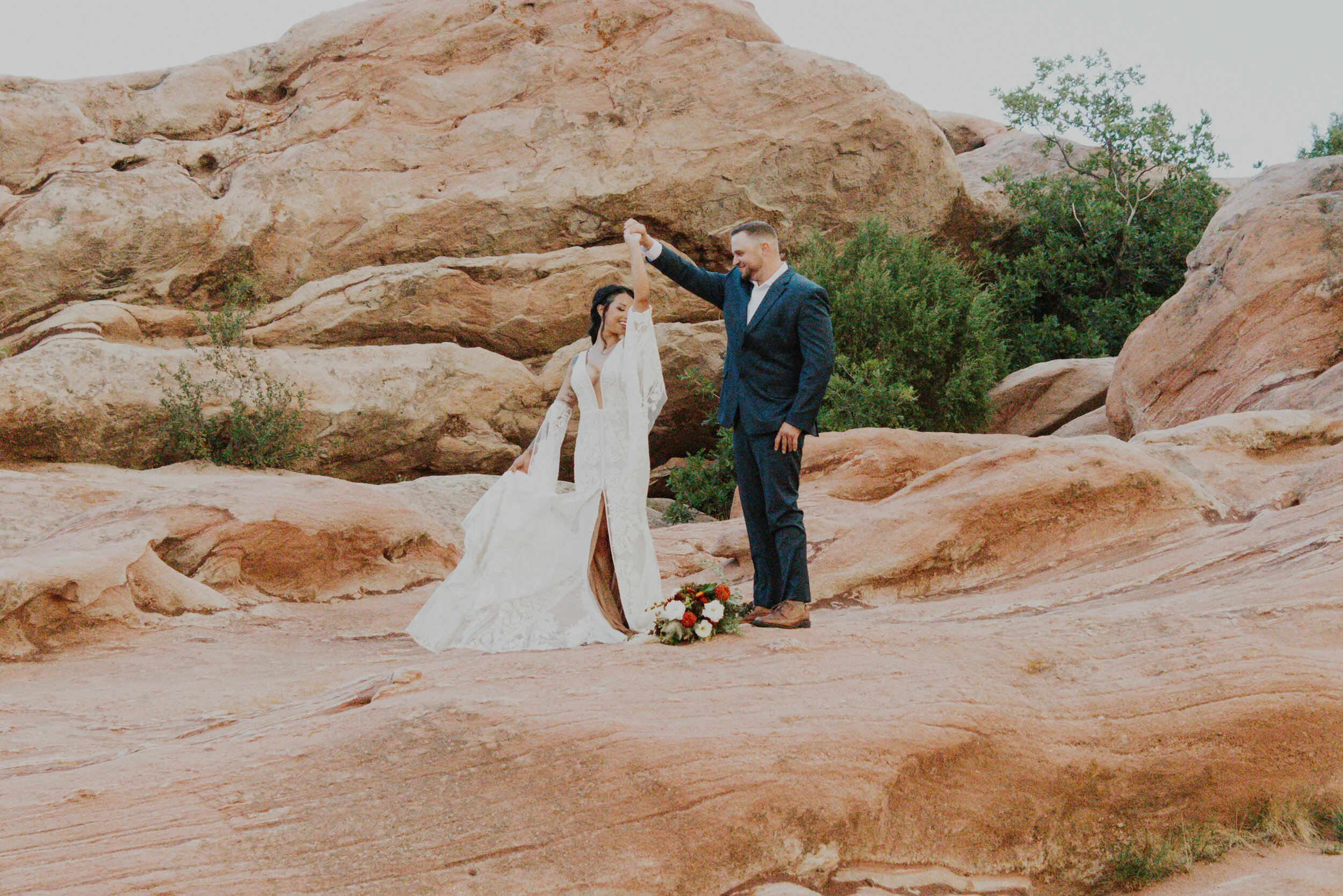 Twirling after their wedding ceremony at Red Rocks, Colorado, Dawn Louise Photography captures candid wedding day moments. bohemian styled lace wedding dress with plunging neckline, bohemian styled wedding sleeves, bride and groom twirling, red rock…