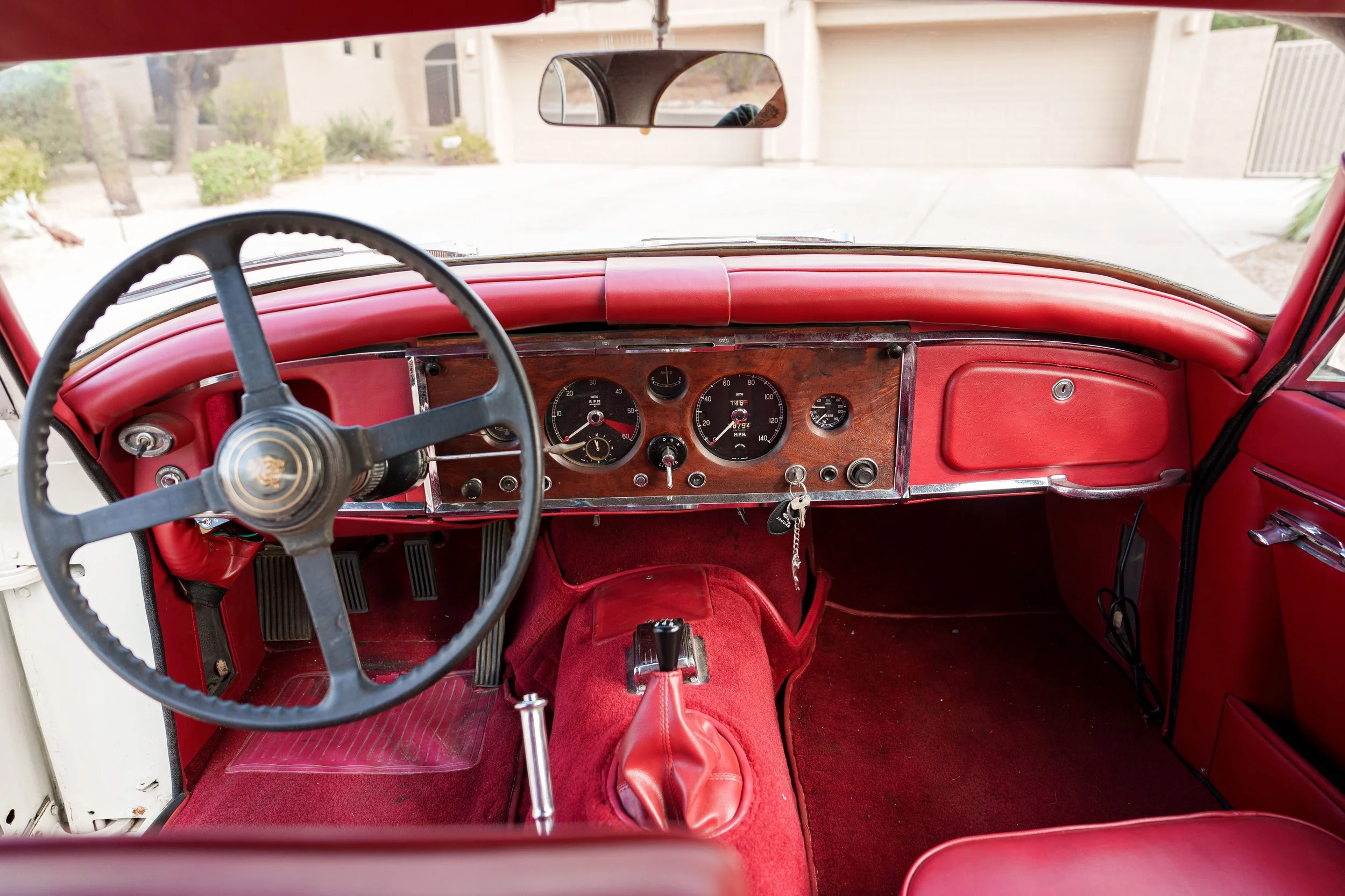 Driver cockpit of a 1960 Jaguar XK150 with red upholstery and wood dashboard