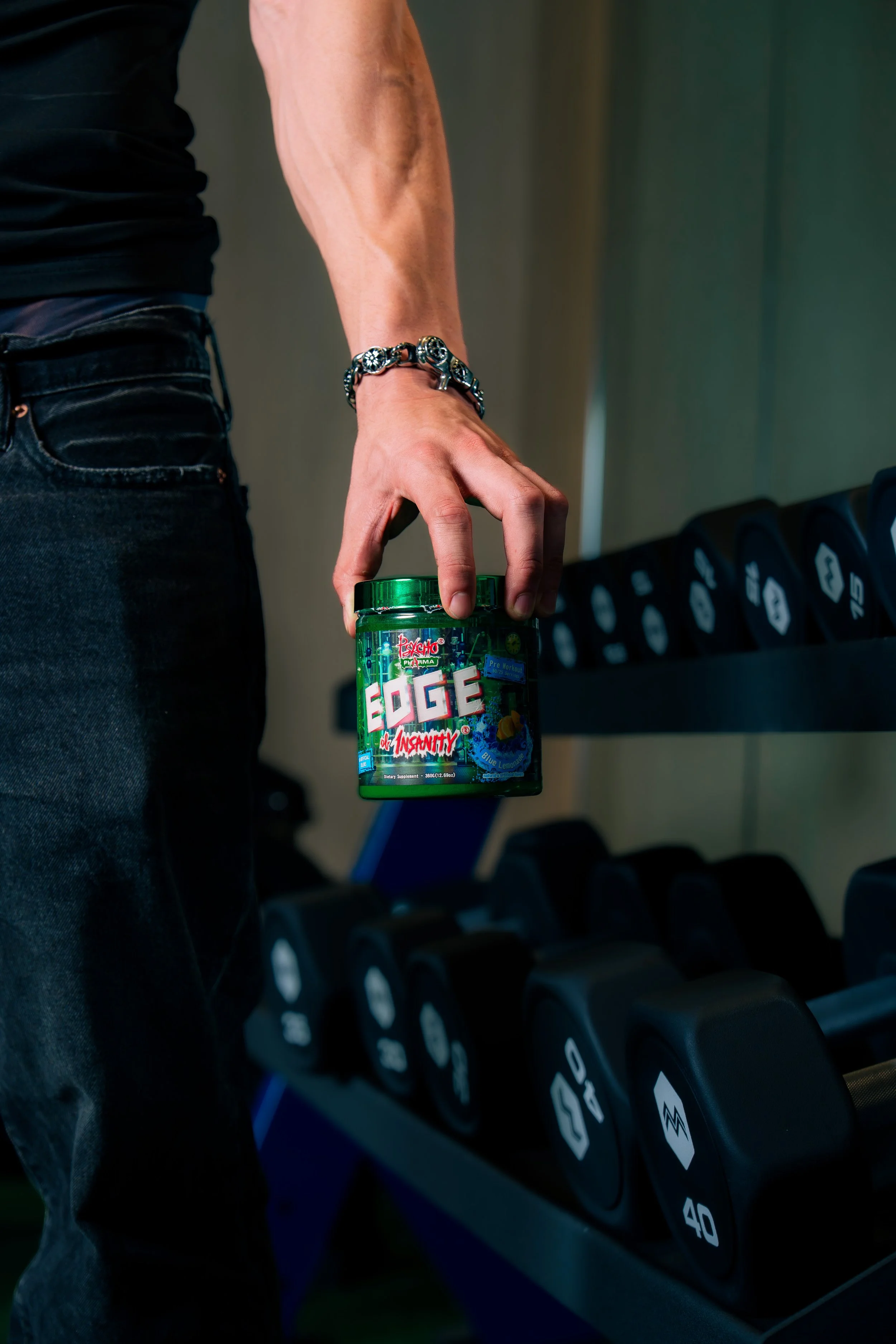 Close-up of a Psycho Pharma supplement held beside a dumbbell rack in a Phoenix gym