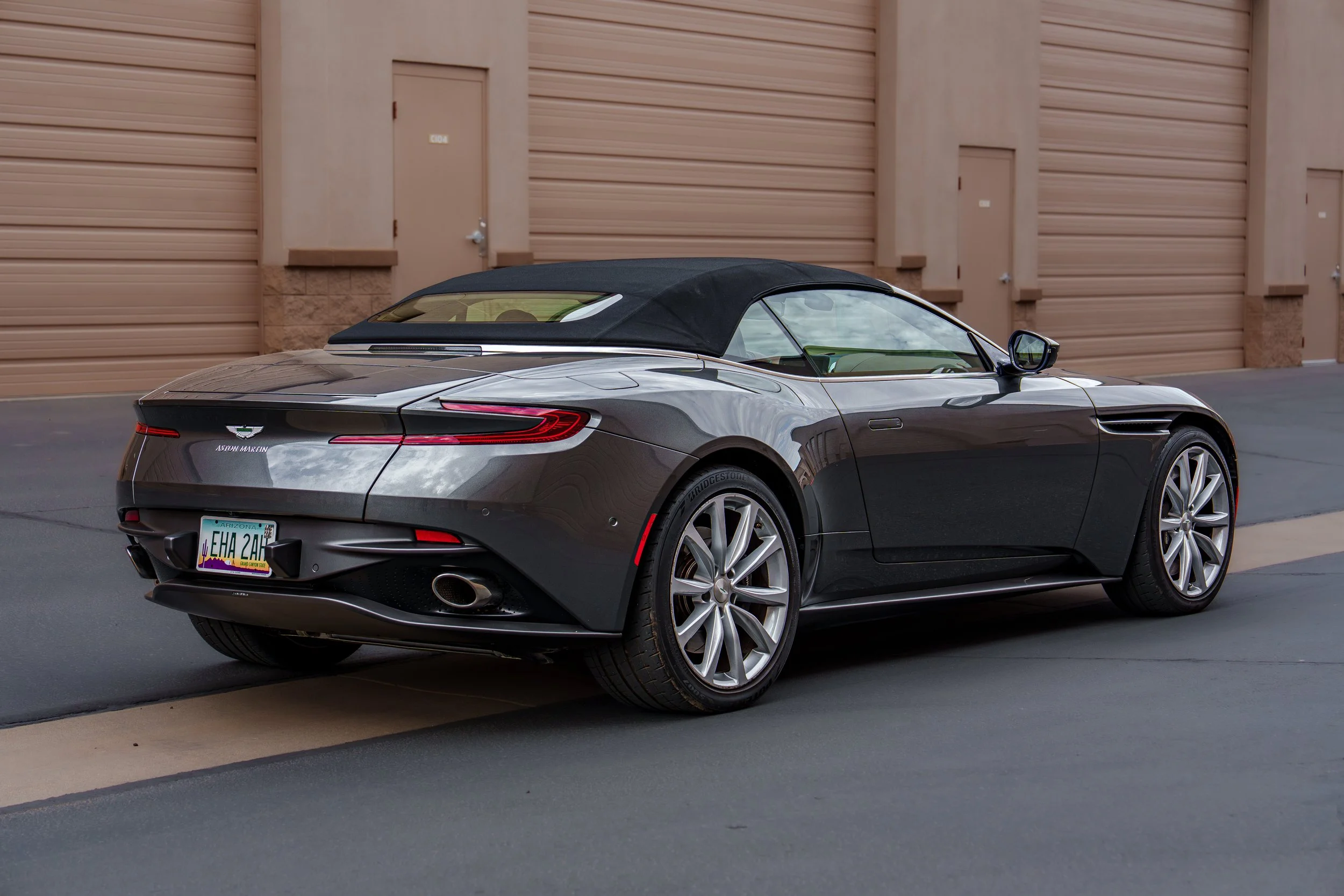Rear three-quarter view of a gray Aston Martin DB11 Volante with black soft top