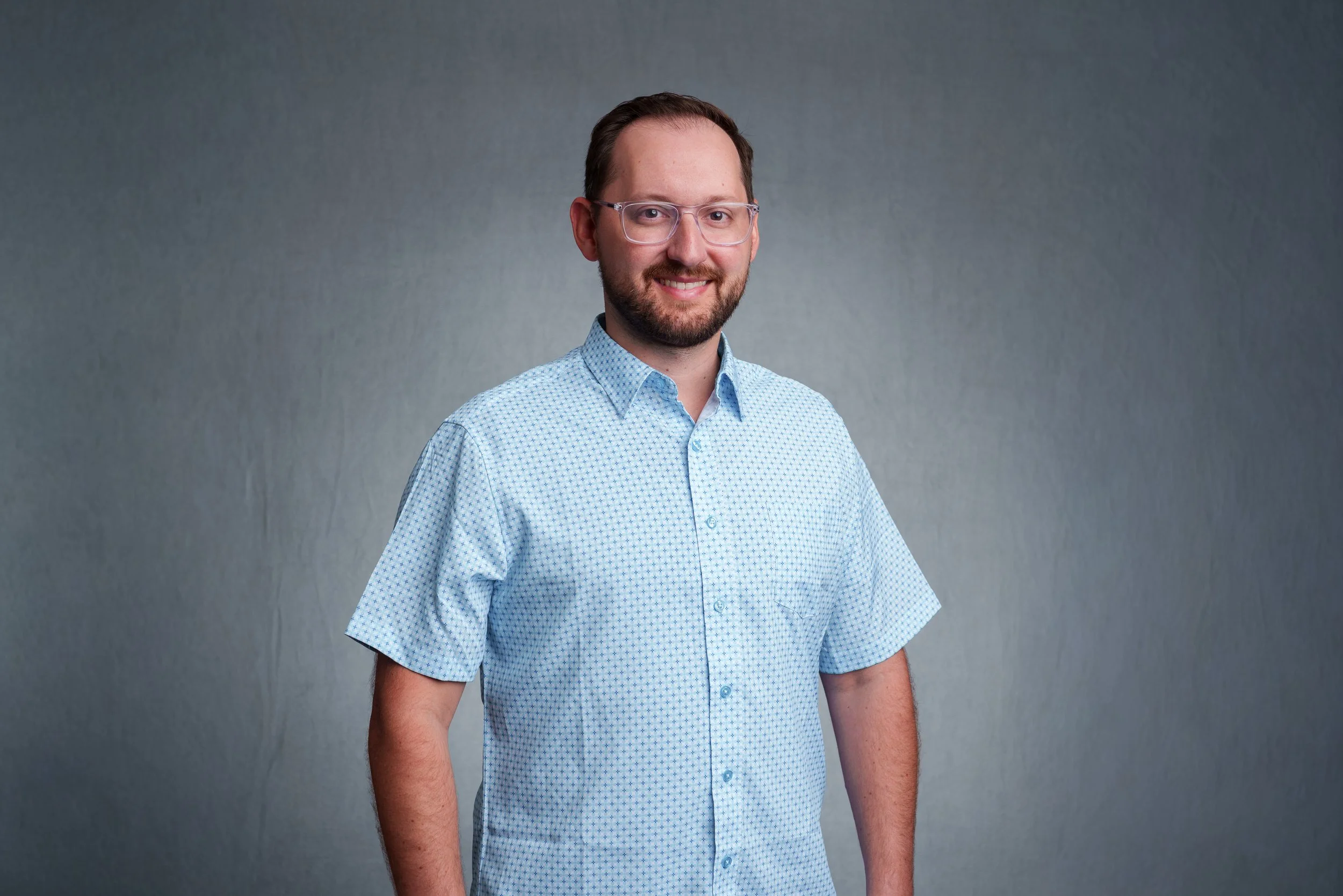 Corporate headshot of a smiling man wearing glasses and a light blue shirt against a gray backdrop in Scottsdale, Arizona.