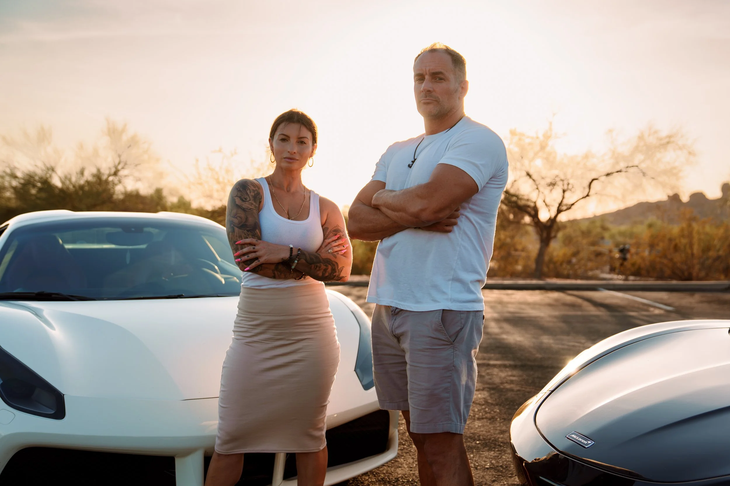 Janelle and Eric posing confidently between two exotic cars during a branding session