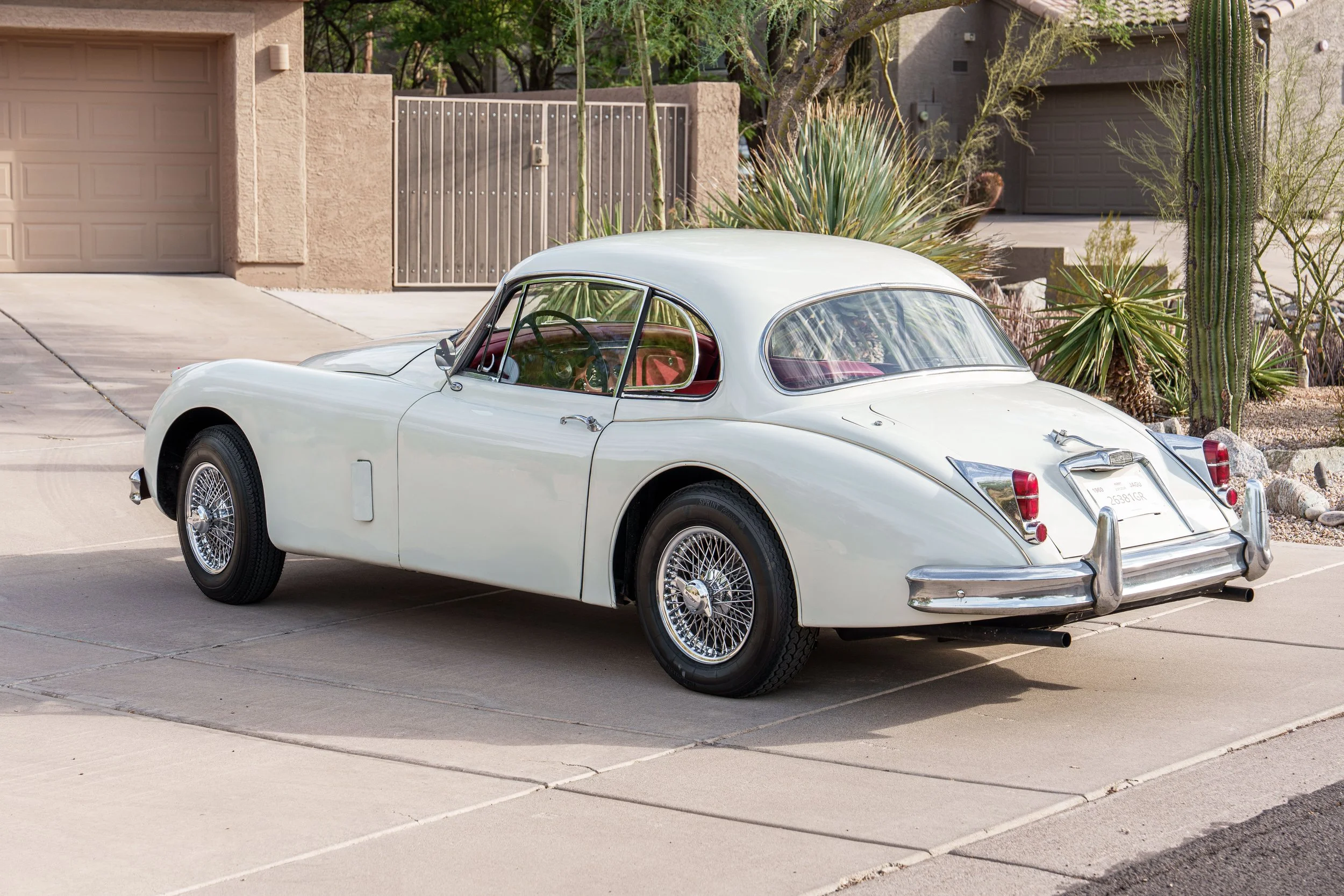 Rear three-quarter view of a white Jaguar XK150 with chrome wire wheels