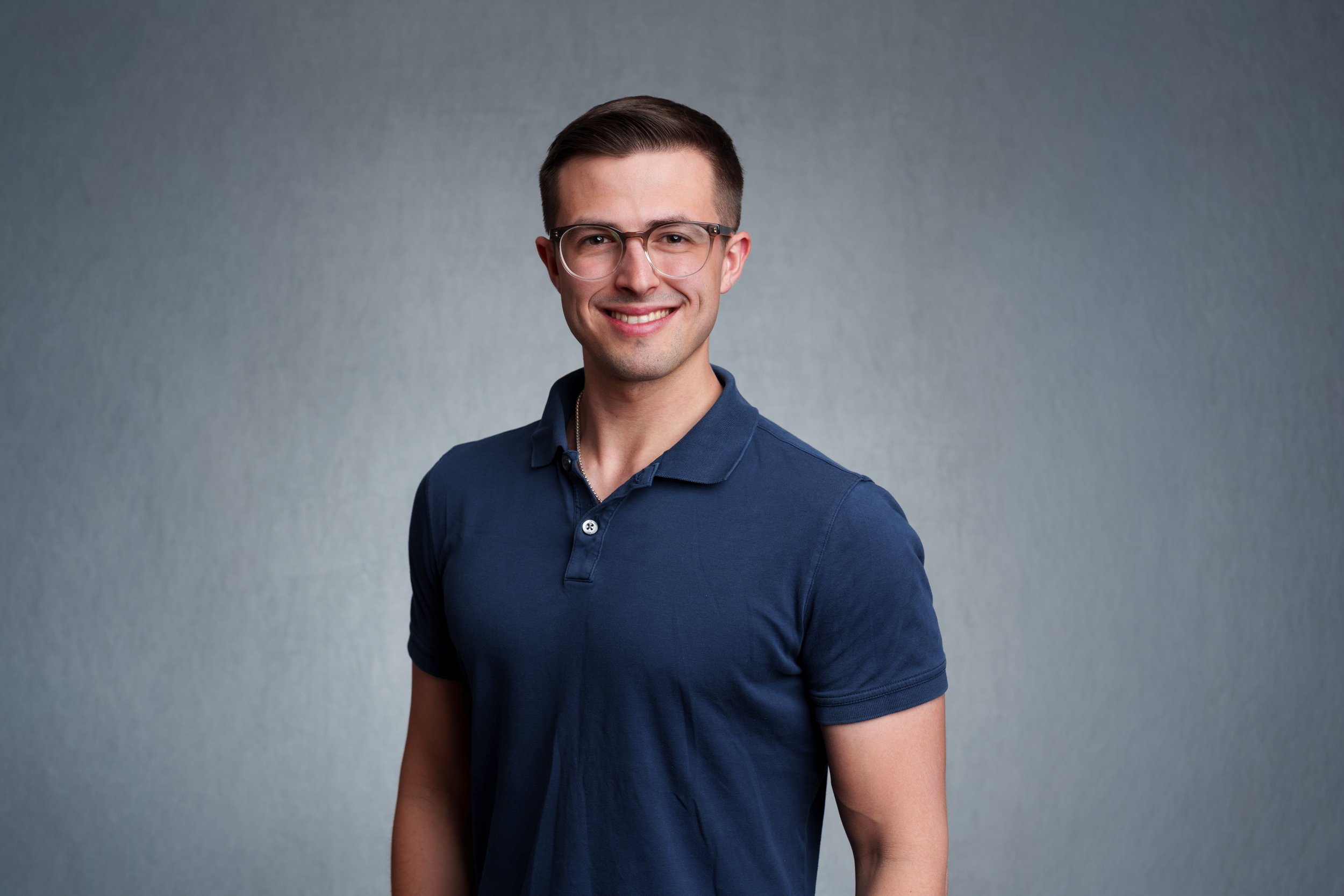Professional business headshot of a smiling man in a navy polo photographed against a gray studio background in Scottsdale.