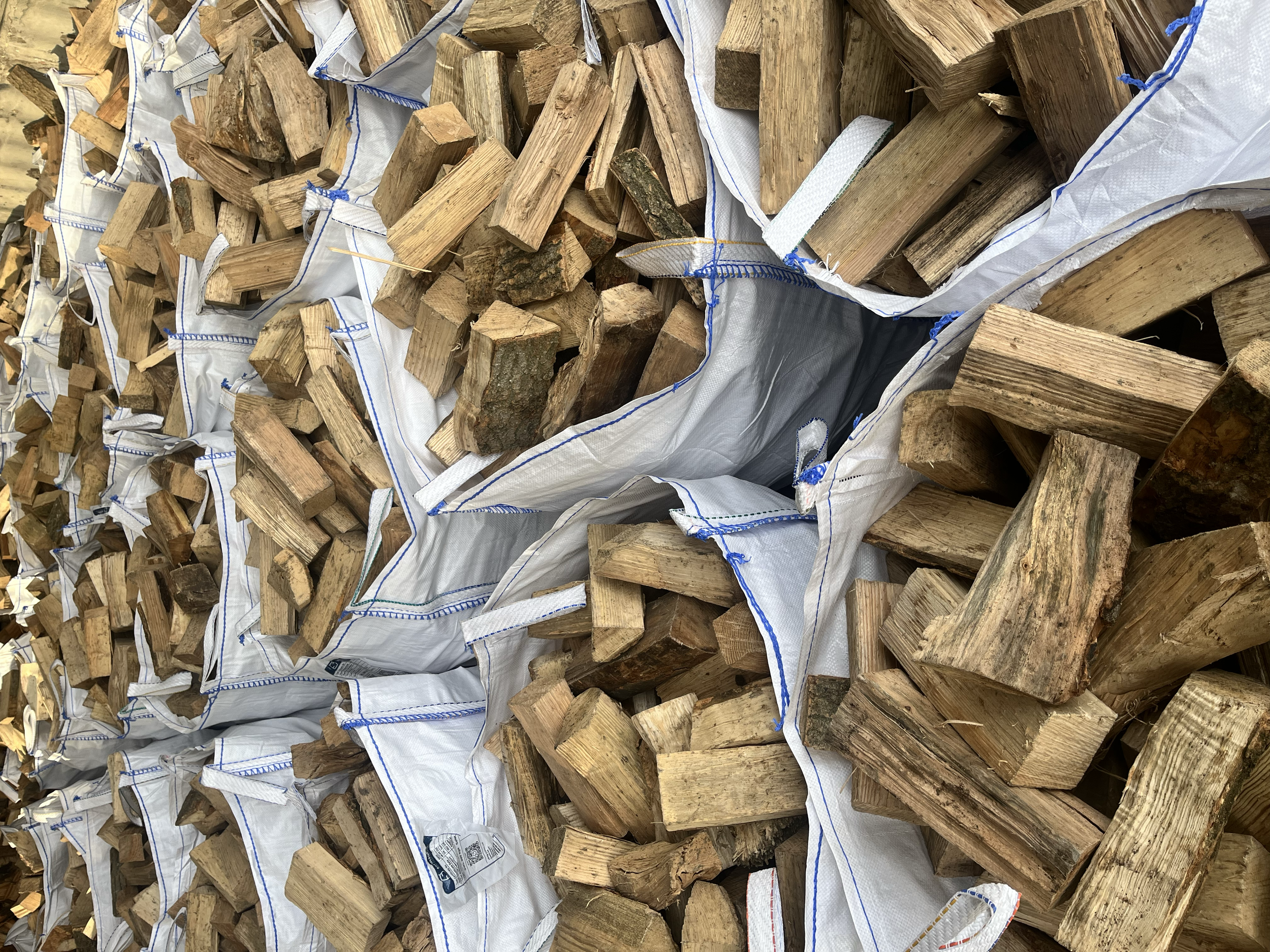 Stacks of chopped wood logs inside large white bags, ready for transport or storage.