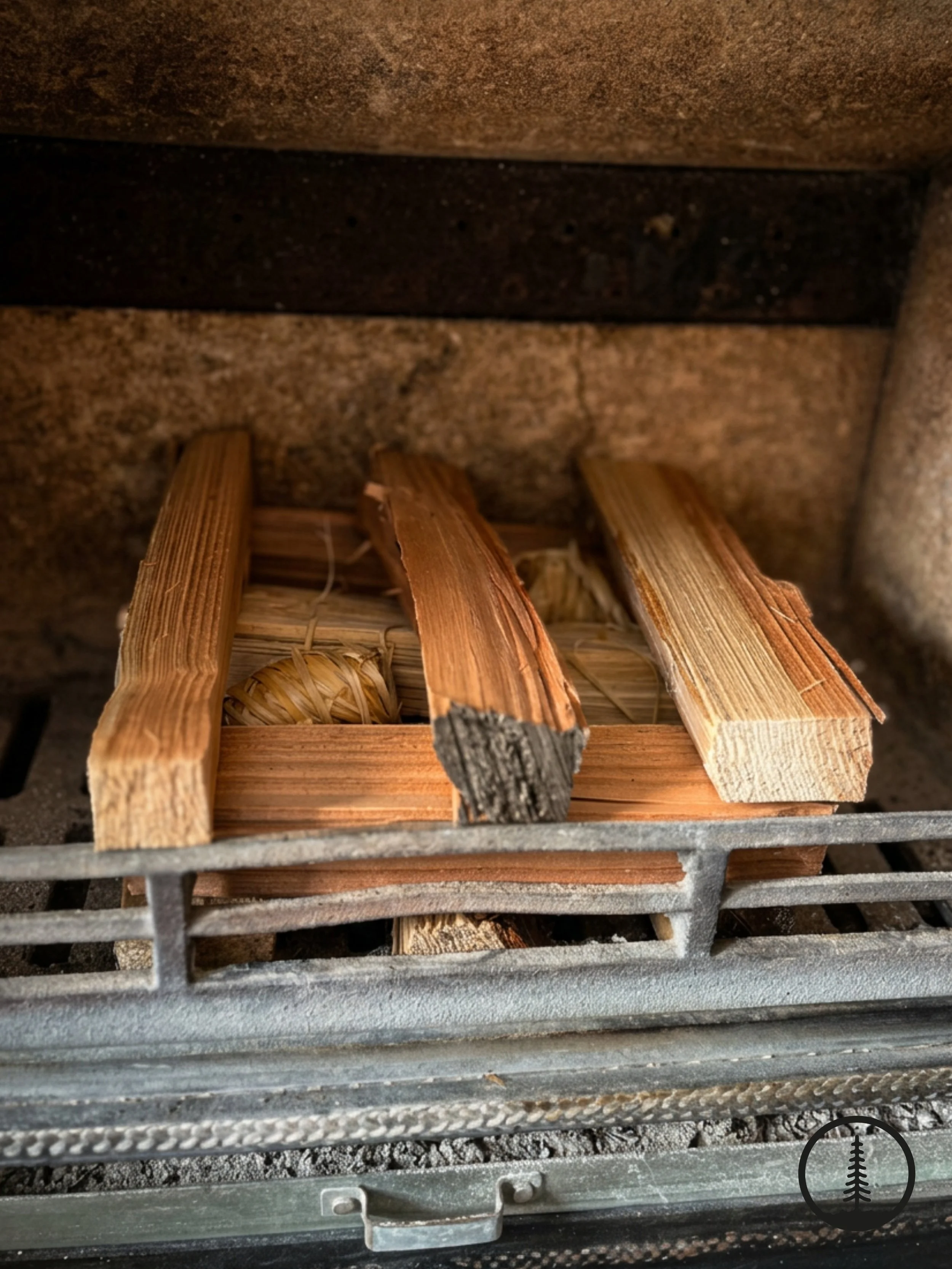 Traditional bottom-up fire lighting method inside a clean log burner, featuring natural wood wool firelighters underneath a raised stack of dry kindling sticks.