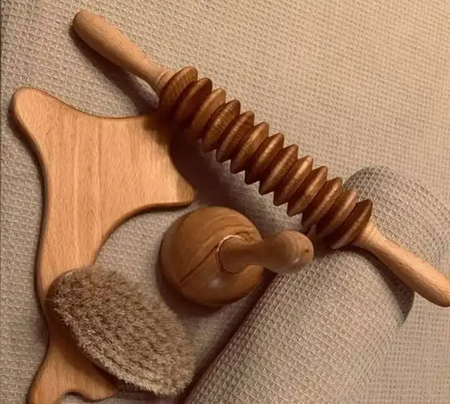 Wooden lymphatic drainage massage tools — roller, gua sha paddle, cup and dry brush — on a soft waffle towel