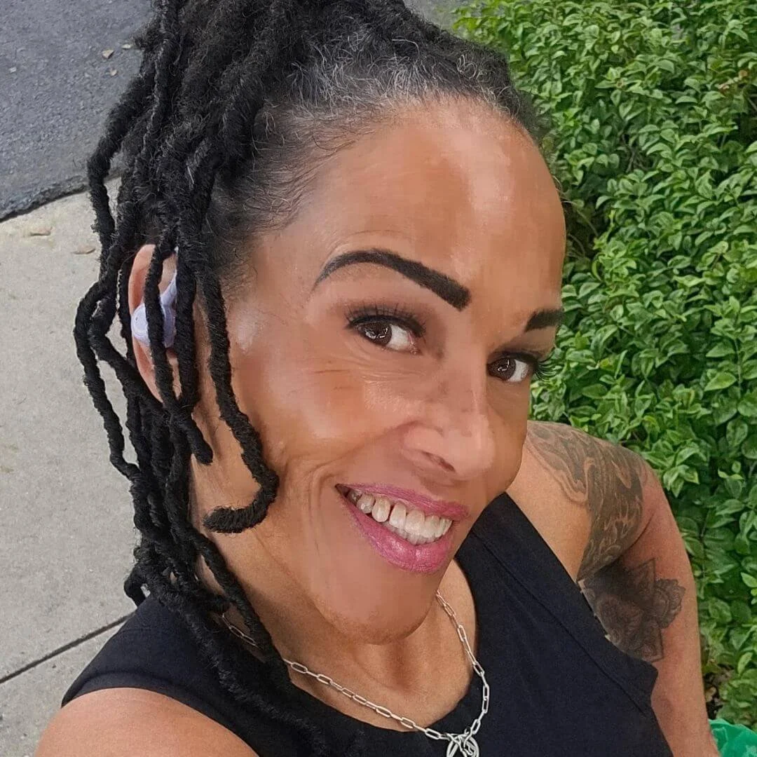 A woman with short dark hair, wearing earrings and a black top, smiling at the camera.