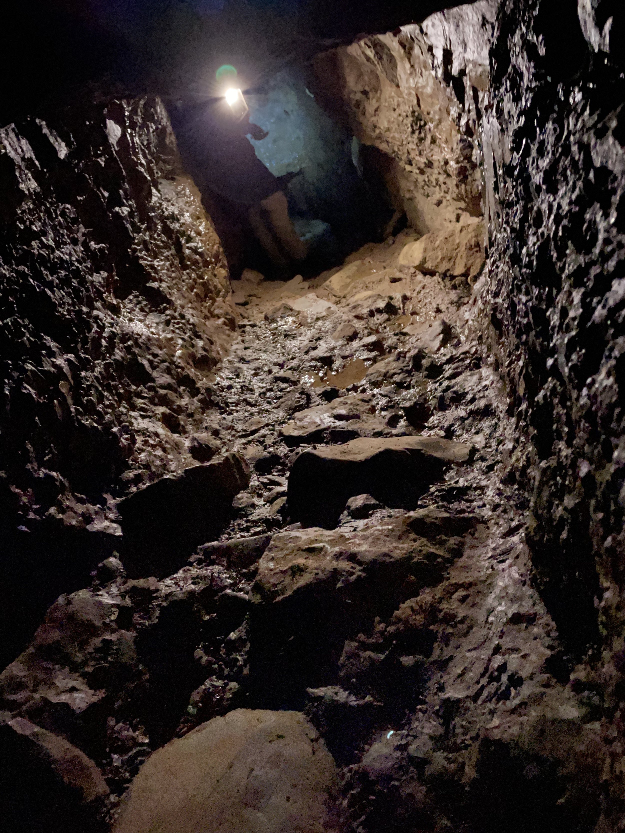 Person exploring a narrow, rocky cave passage with a flashlight
