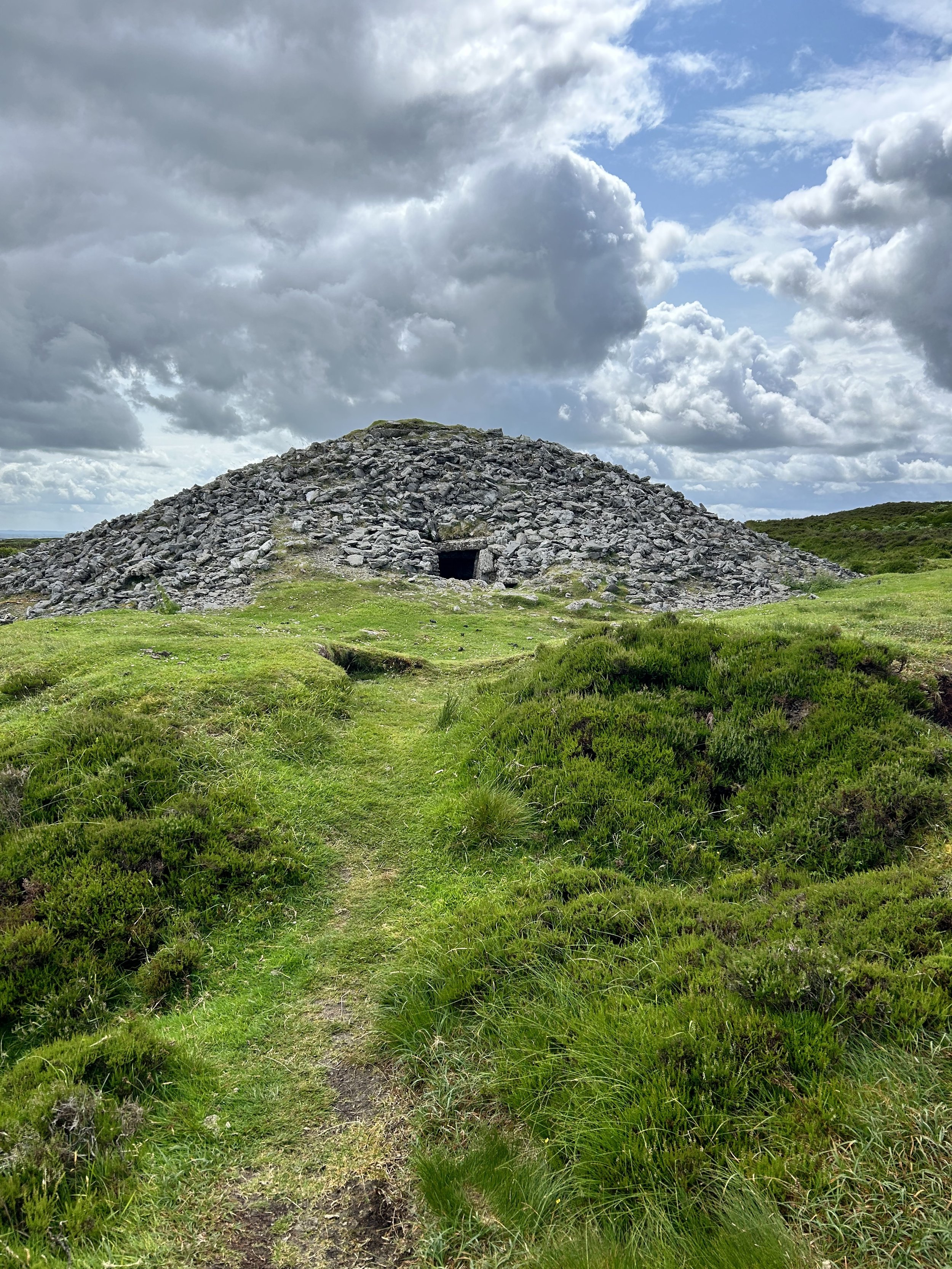 Stone cairn on grassy hill under cloudy sky