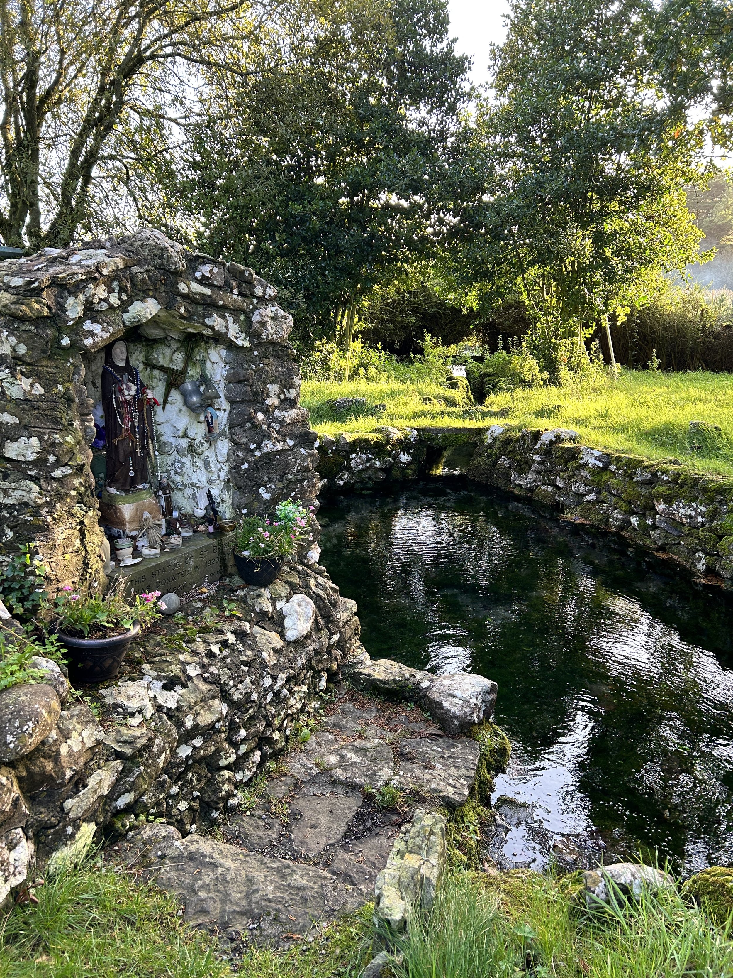A stone structure with religious statues and a small pond surrounded by greenery.
