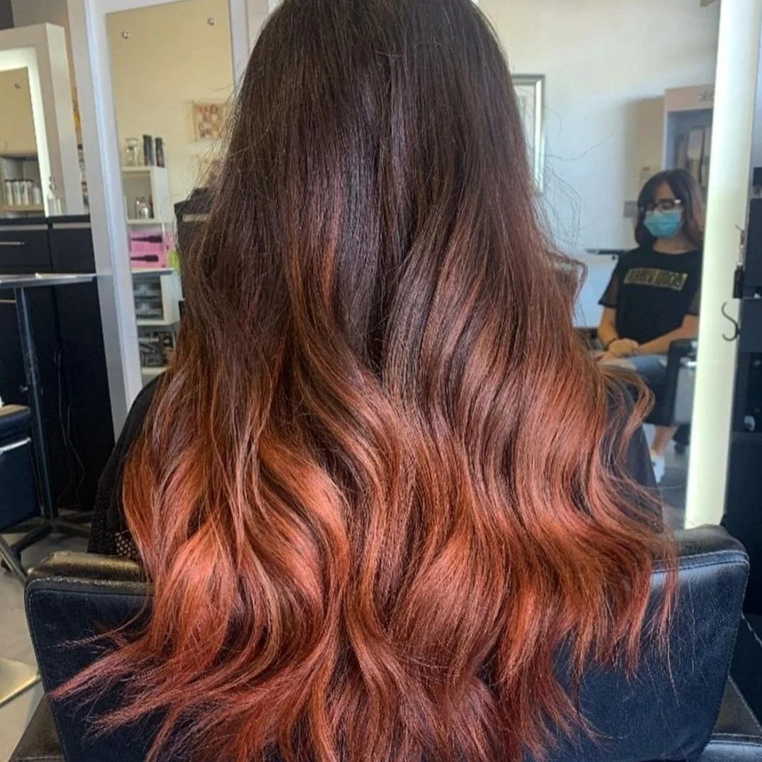 Woman with long, wavy, ombre hair transitioning from dark brown to reddish-brown