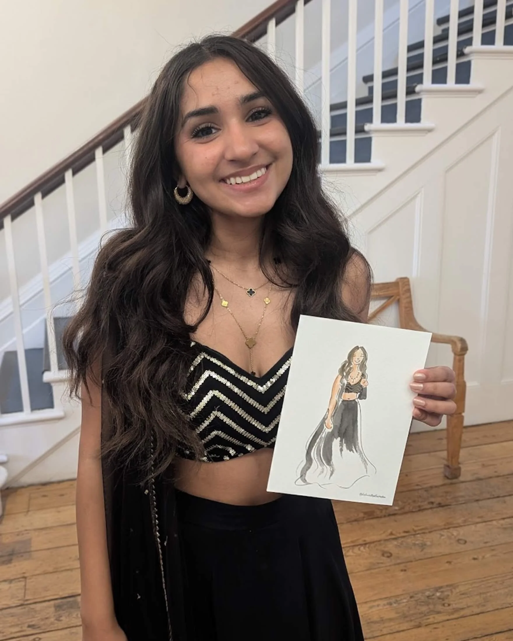 A woman in a black crop top and skirt holding a live illustration of herself
