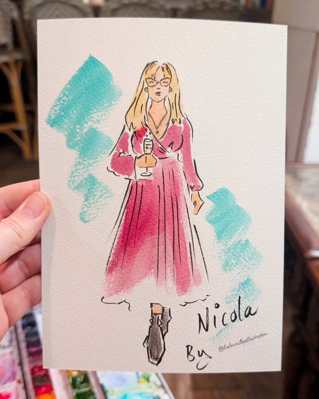 Custom watercolour portrait of a lady with blonde hair and pink dress holding wine illustrated by Helen Ridley