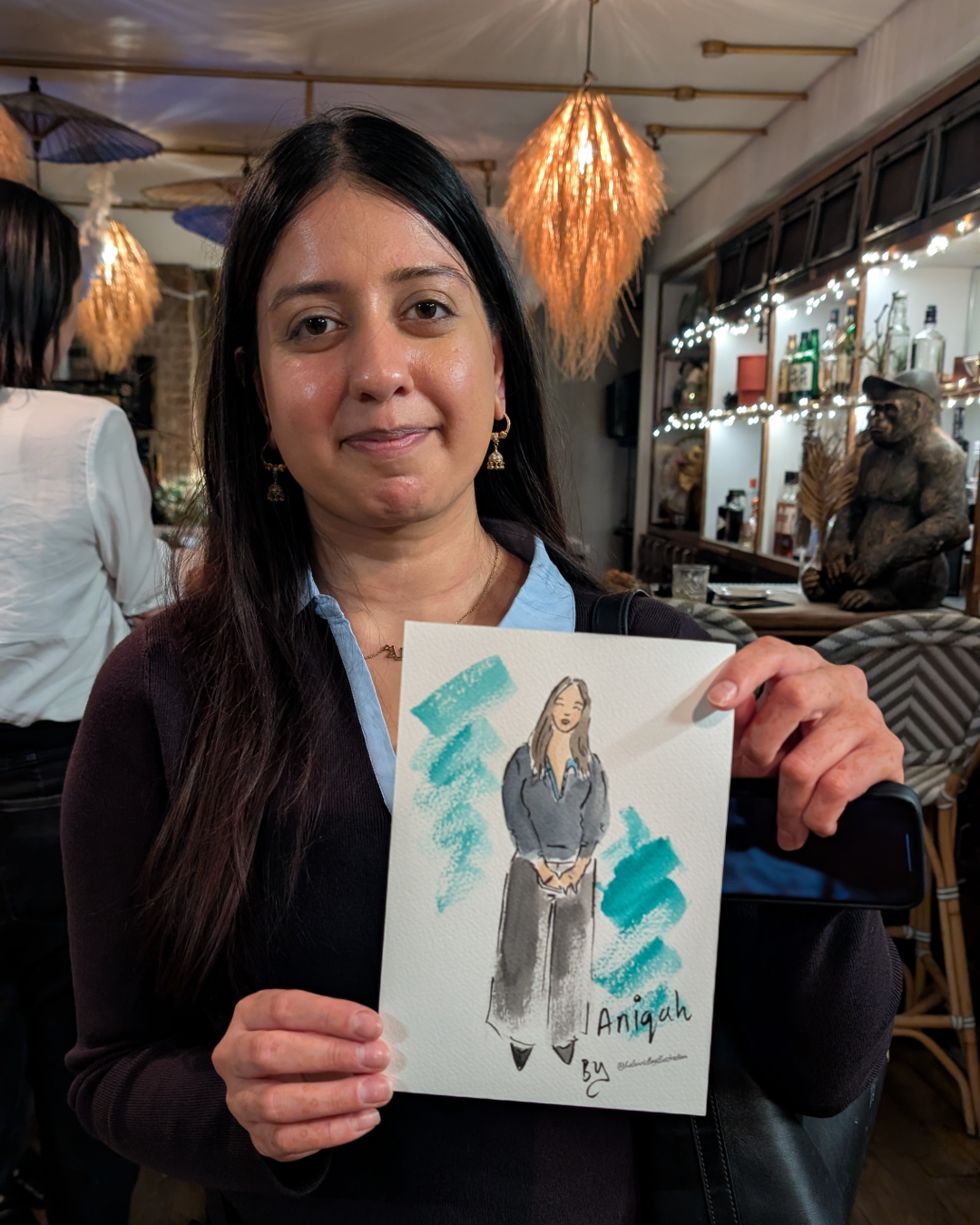Lady smiling while holding a watercolour portrait of herself at a networking event