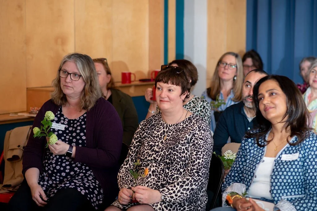 A group of ladies sitting on chairs smiling and taking part in a public speaking event at the creative networking event reading