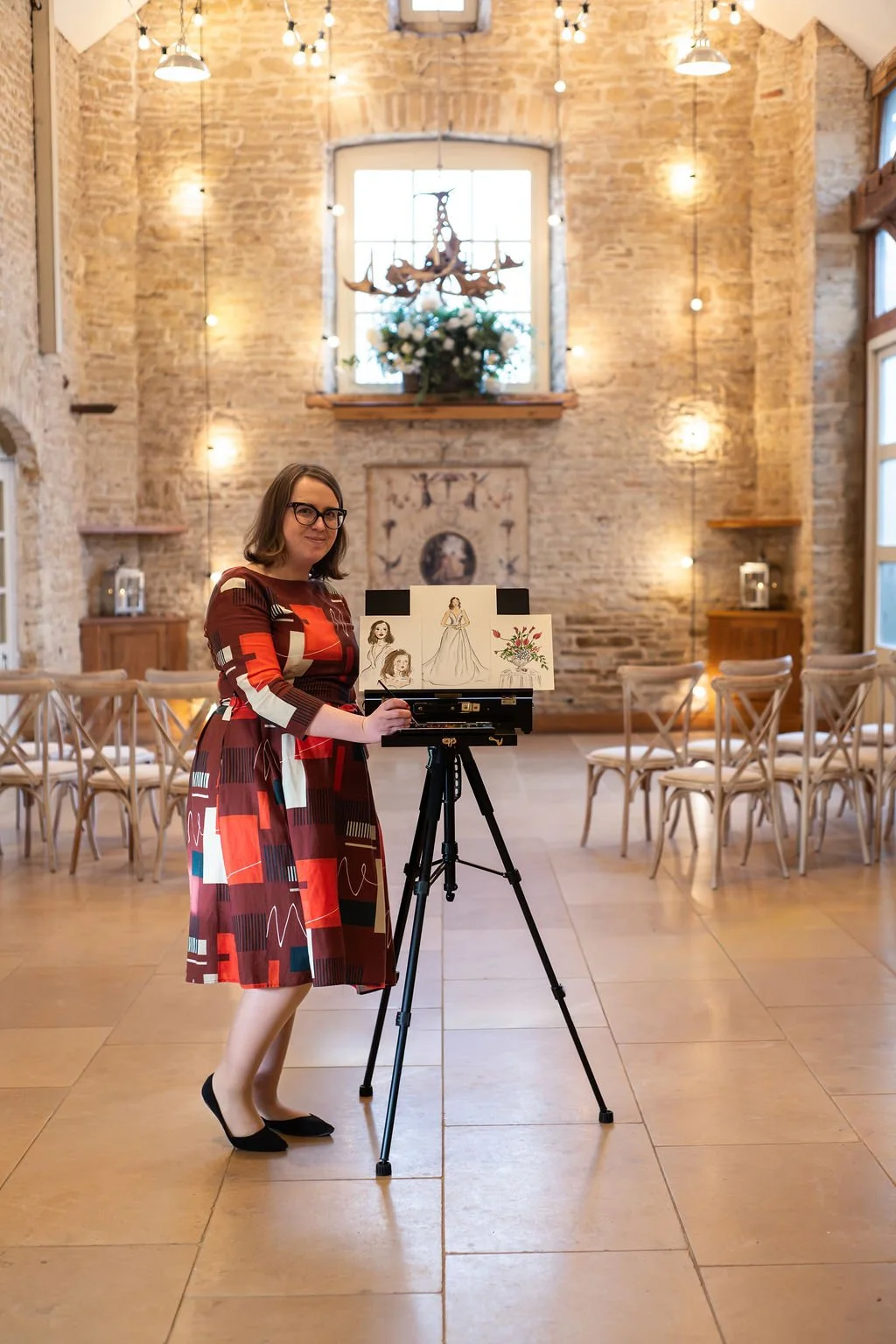 Illustrator Helen Ridley stood inside a wedding venue wearing patterned dress next to her illustrations
