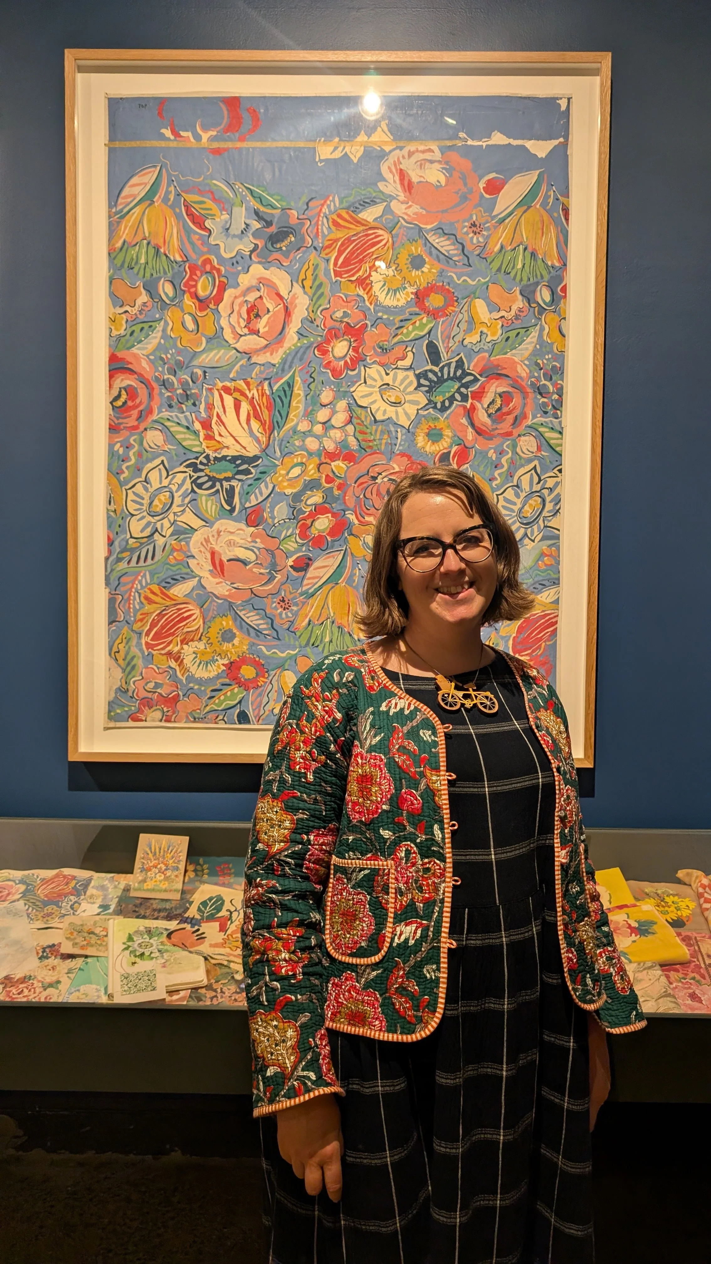 Illustrator Helen Ridley smiling and standing in front of a framed colourful flower illustration by textile artist Sarah Campbell