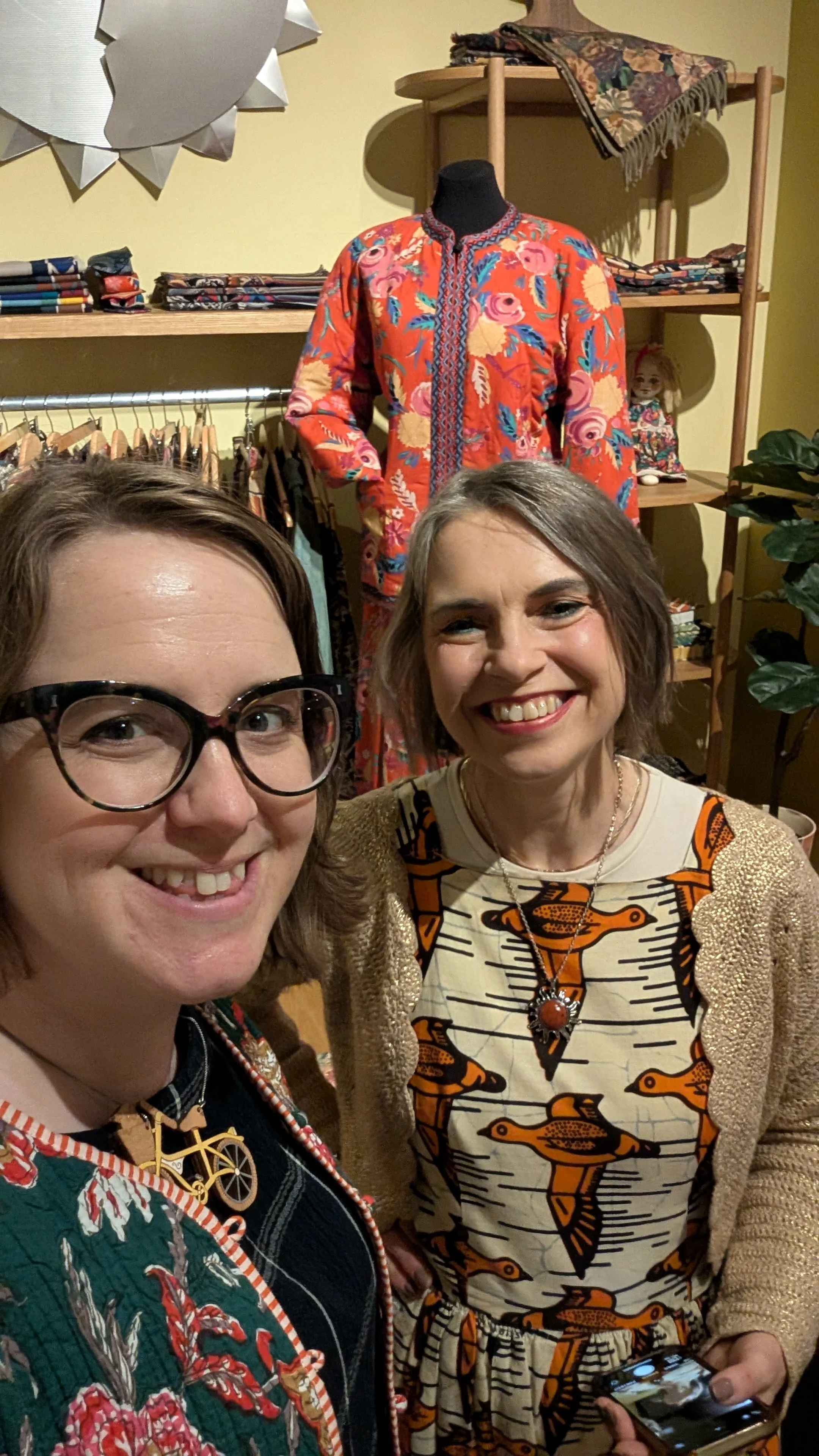 Illustrators Helen Ridley and Zoe Parker smiling and standing in front of a floral patterned jacket at the Paint Pattern Print exhibition in London