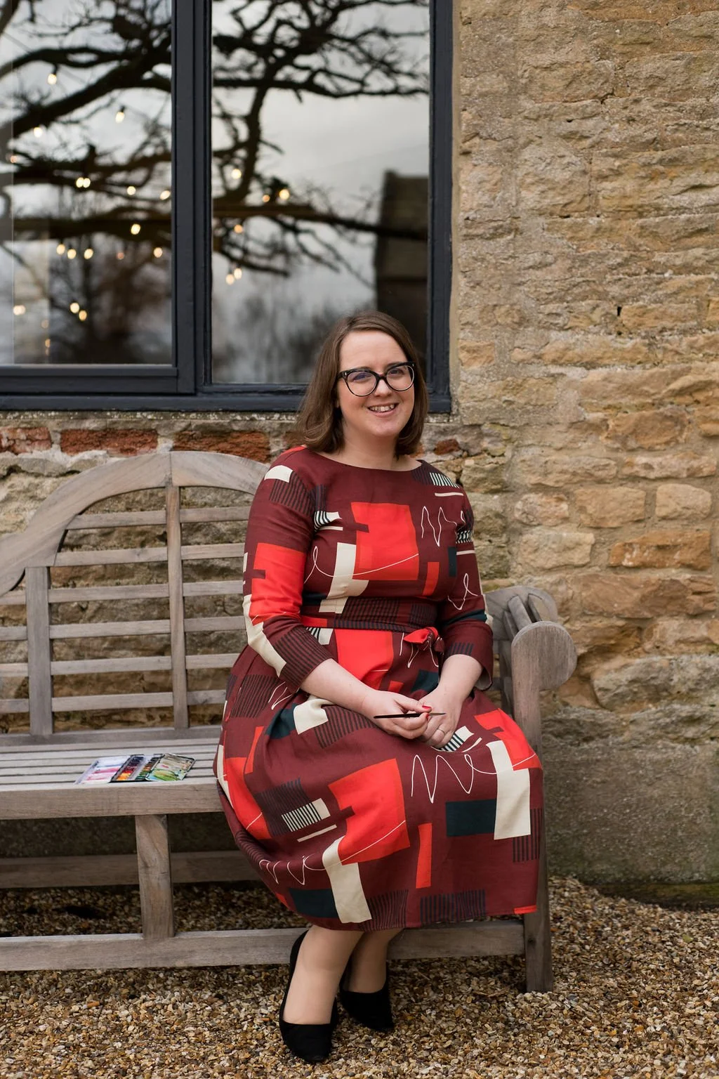 Photo of illustrator Helen RIdley sitting on a bench next to a paint palette at Merriscourt, a wedding venue in the cotswolds. Photo by Nicola Benson