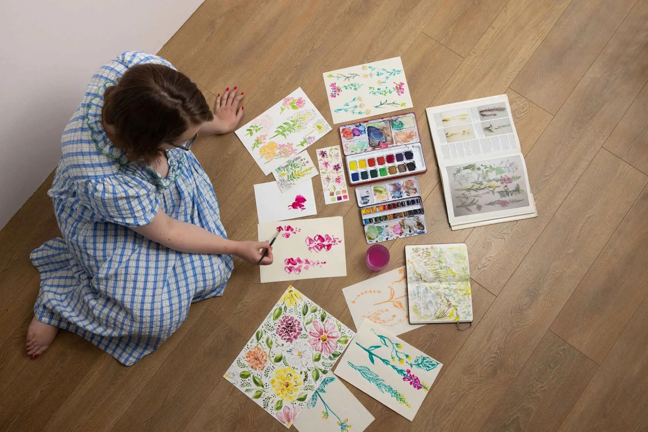 Helen Ridley sat on the floor, surrounded by watercolour illustrations