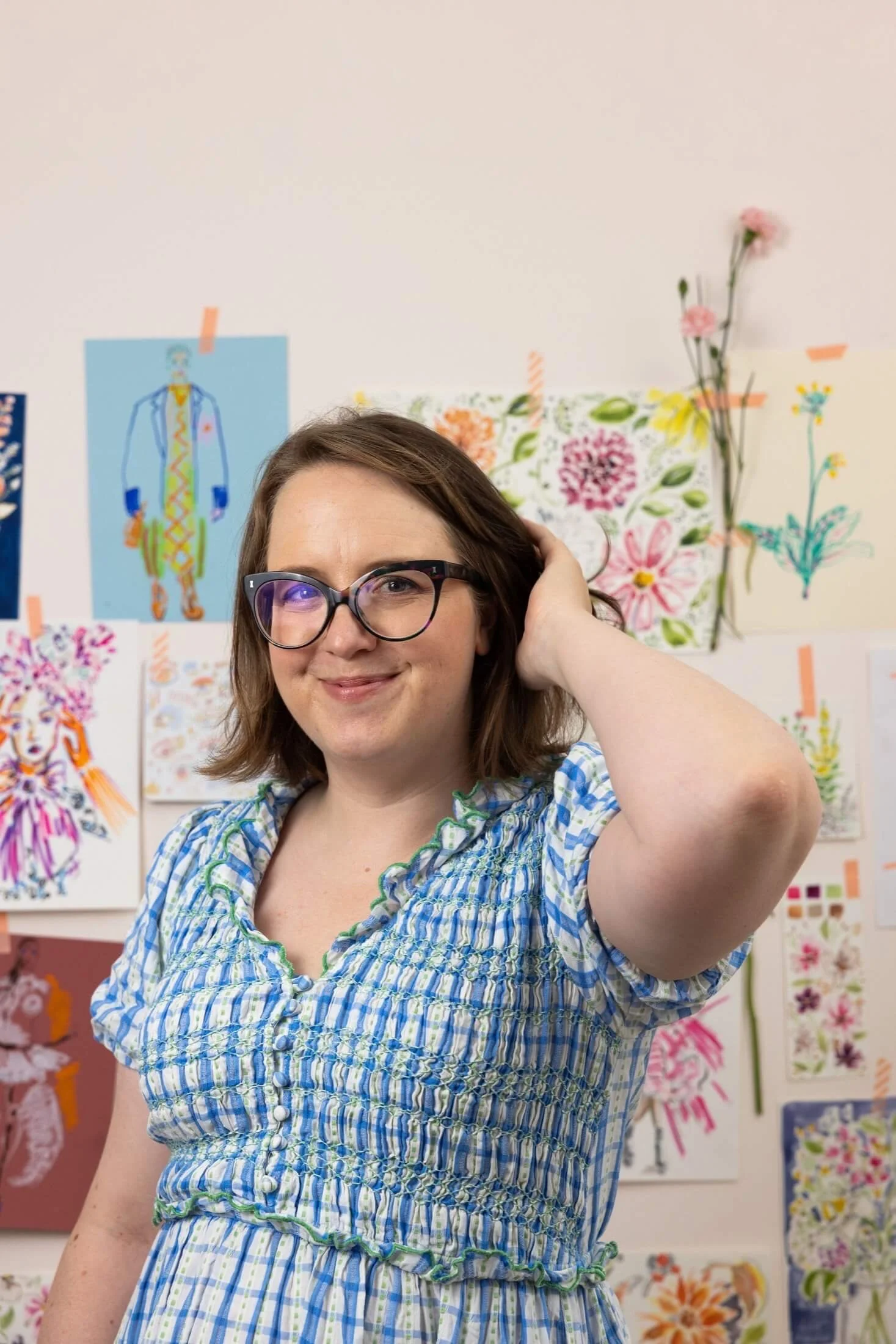 Helen Ridley smiling at the camera, stood in front of a wall of her illustrations