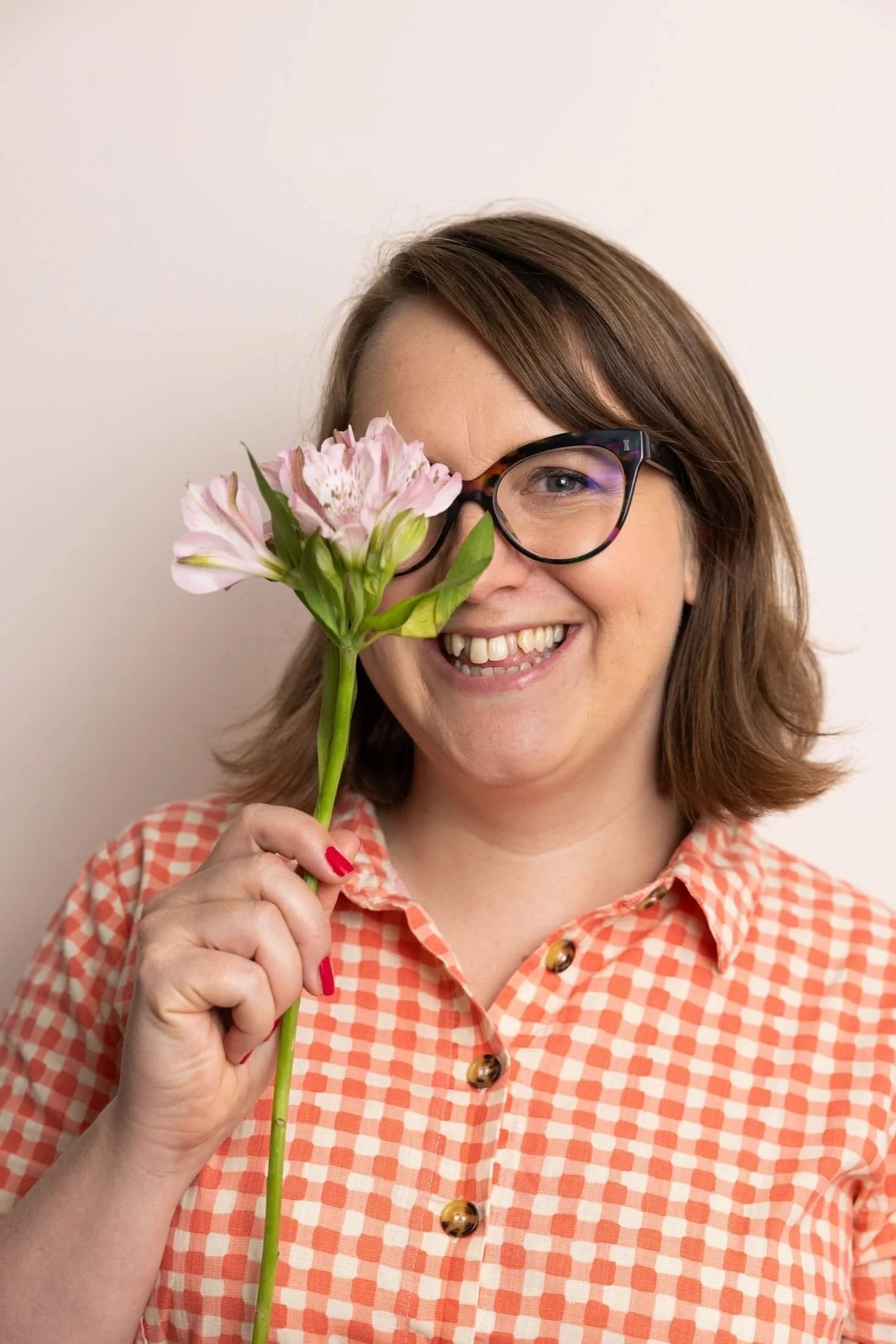 Helen Ridley smiling whilst peeking around a pink flower