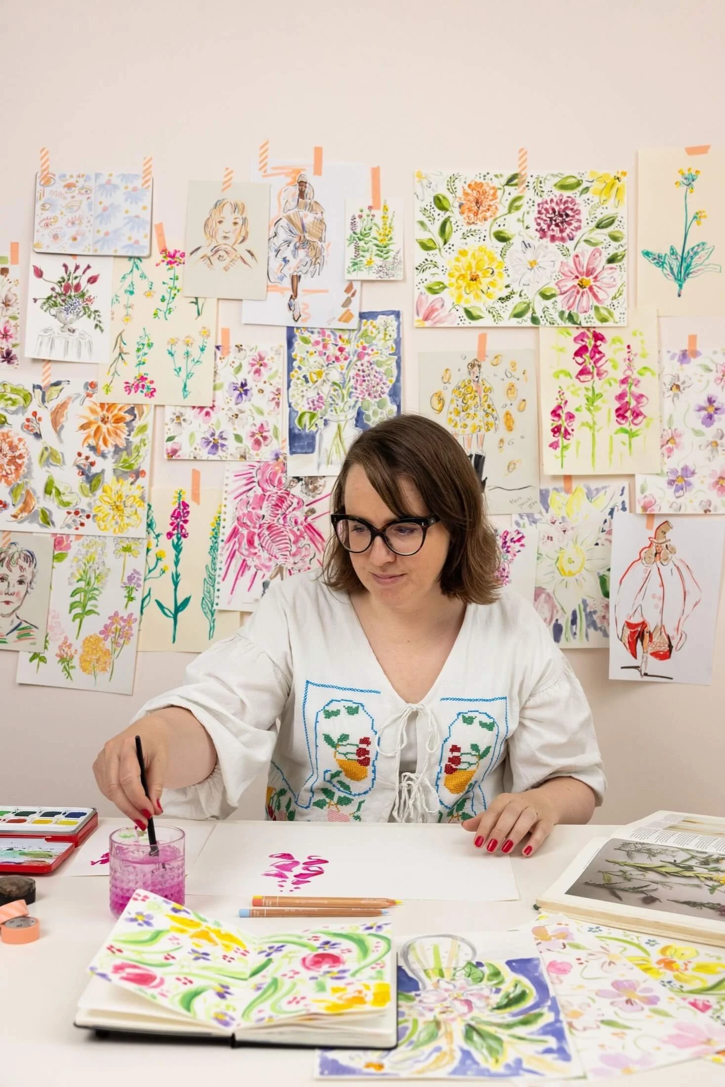 Helen Ridley watercolour painting at a desk, with illustrations behind her