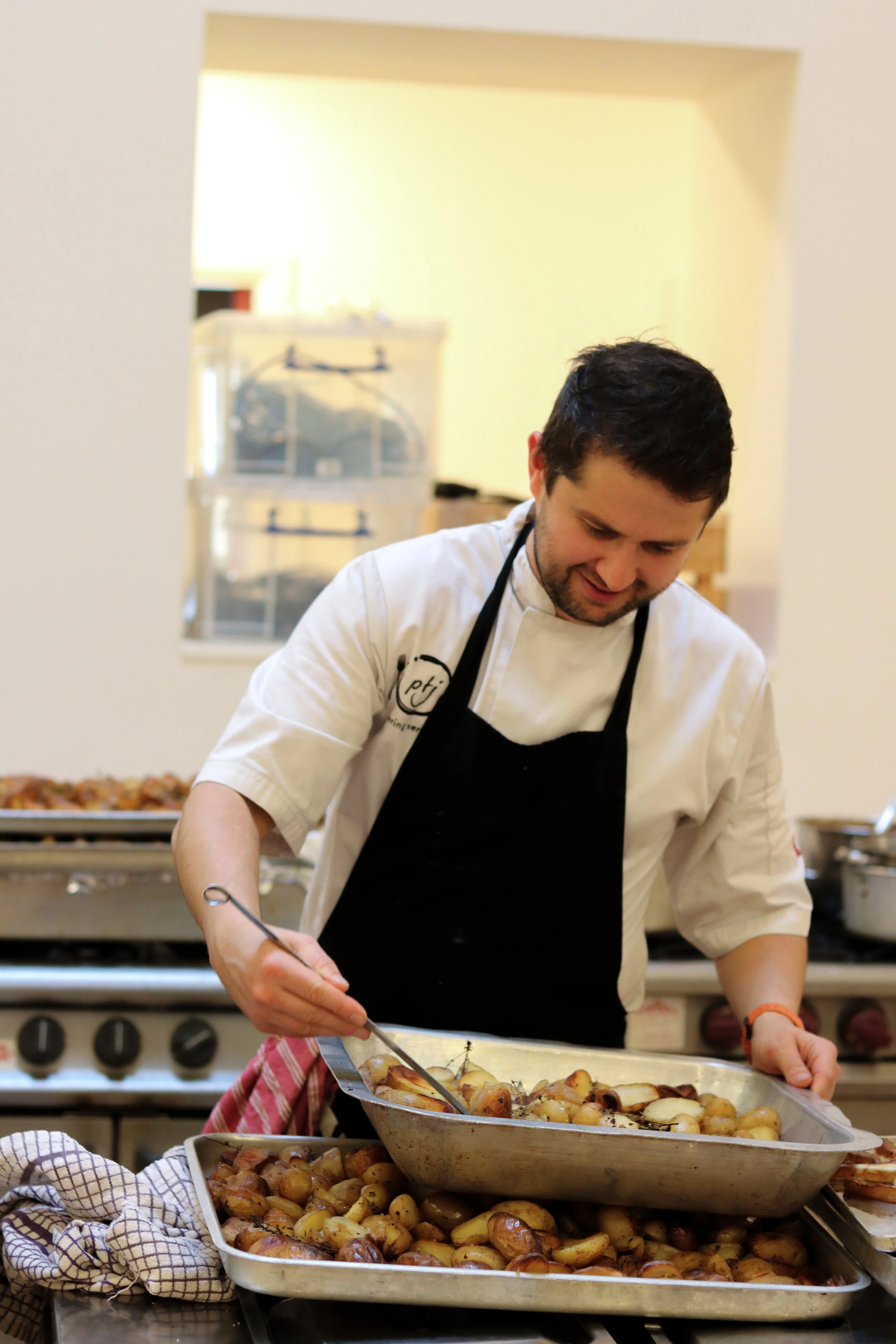 Chef arranging roasted potatoes on a tray, with more roasted potatoes behind him in a commercial kitchen.