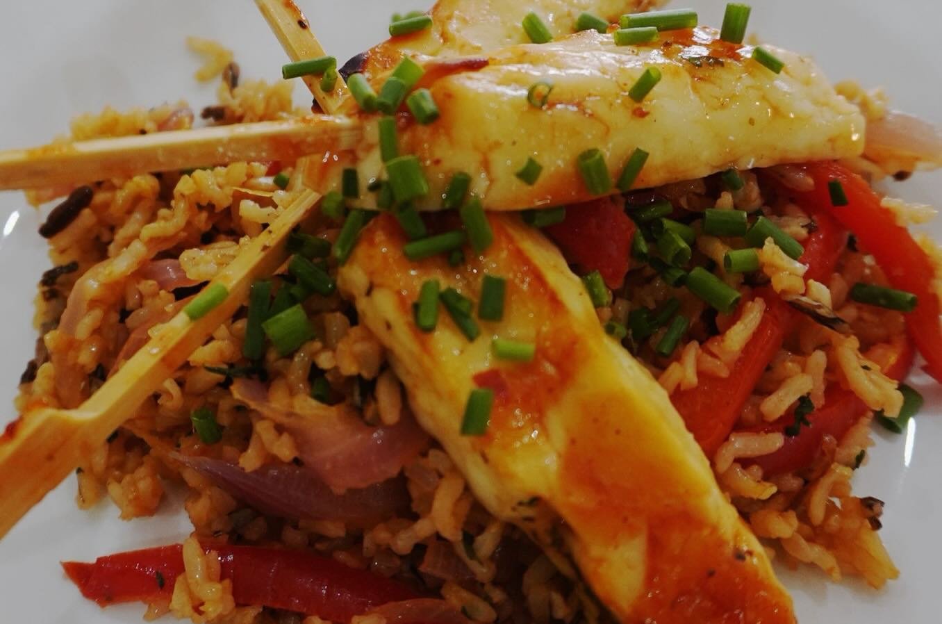 Plate of fried rice with vegetables, topped with fried eggs garnished with chopped green onions.