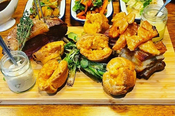 Assorted fried foods, vegetables, and dips on a wooden tray, including fried chicken, fried green beans, small jars of creamy sauces, and side salads in bowls.
