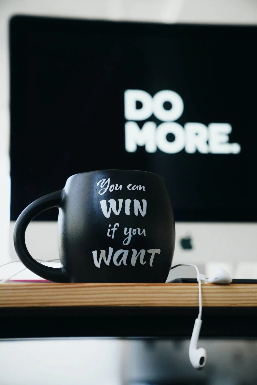 black mug sitting on top of wooden desk with drooping earphone saying "you can win if you want"