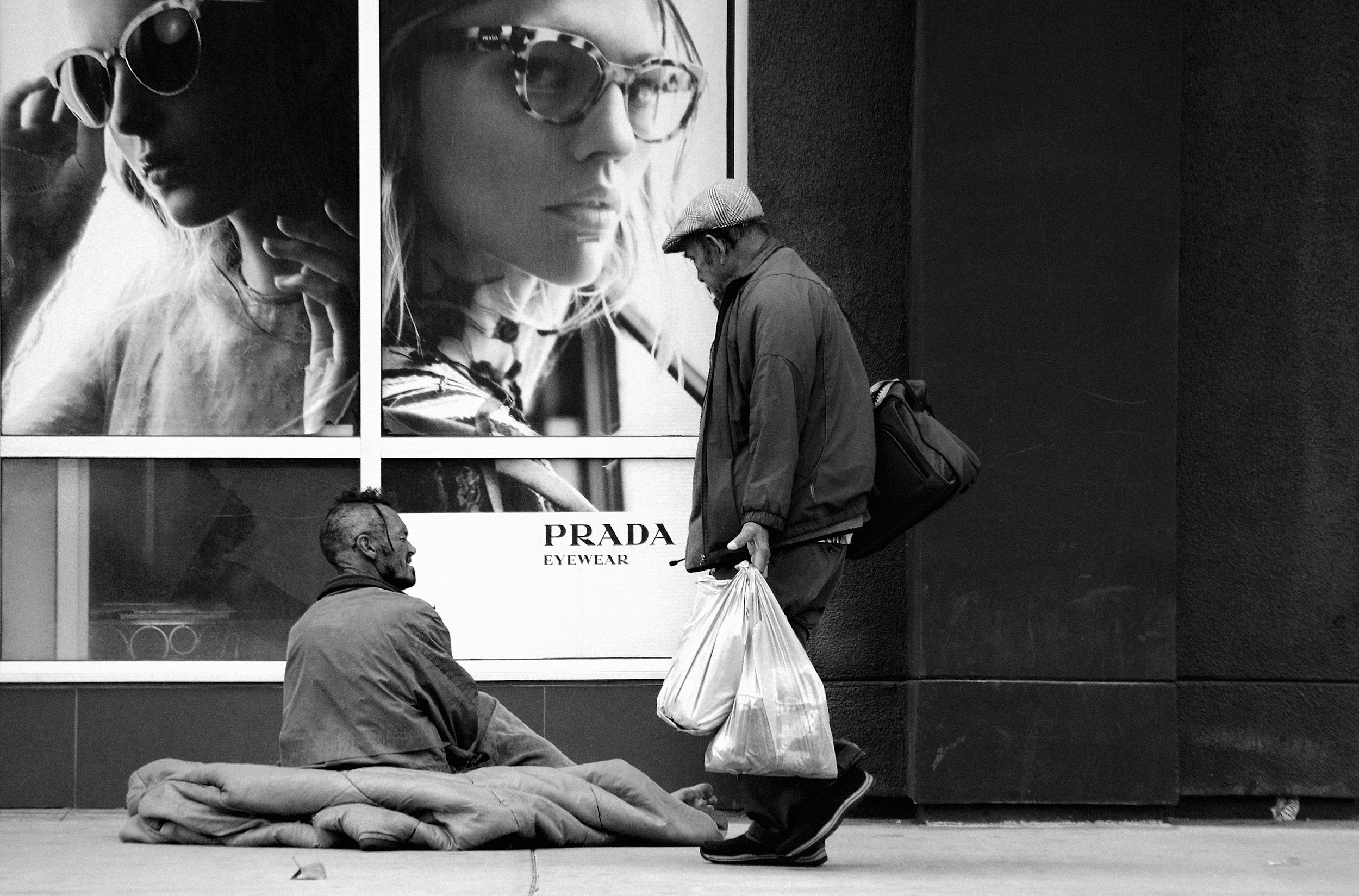 homeless person sitting on ground with blankt infront of prada eyewear luxury campaign