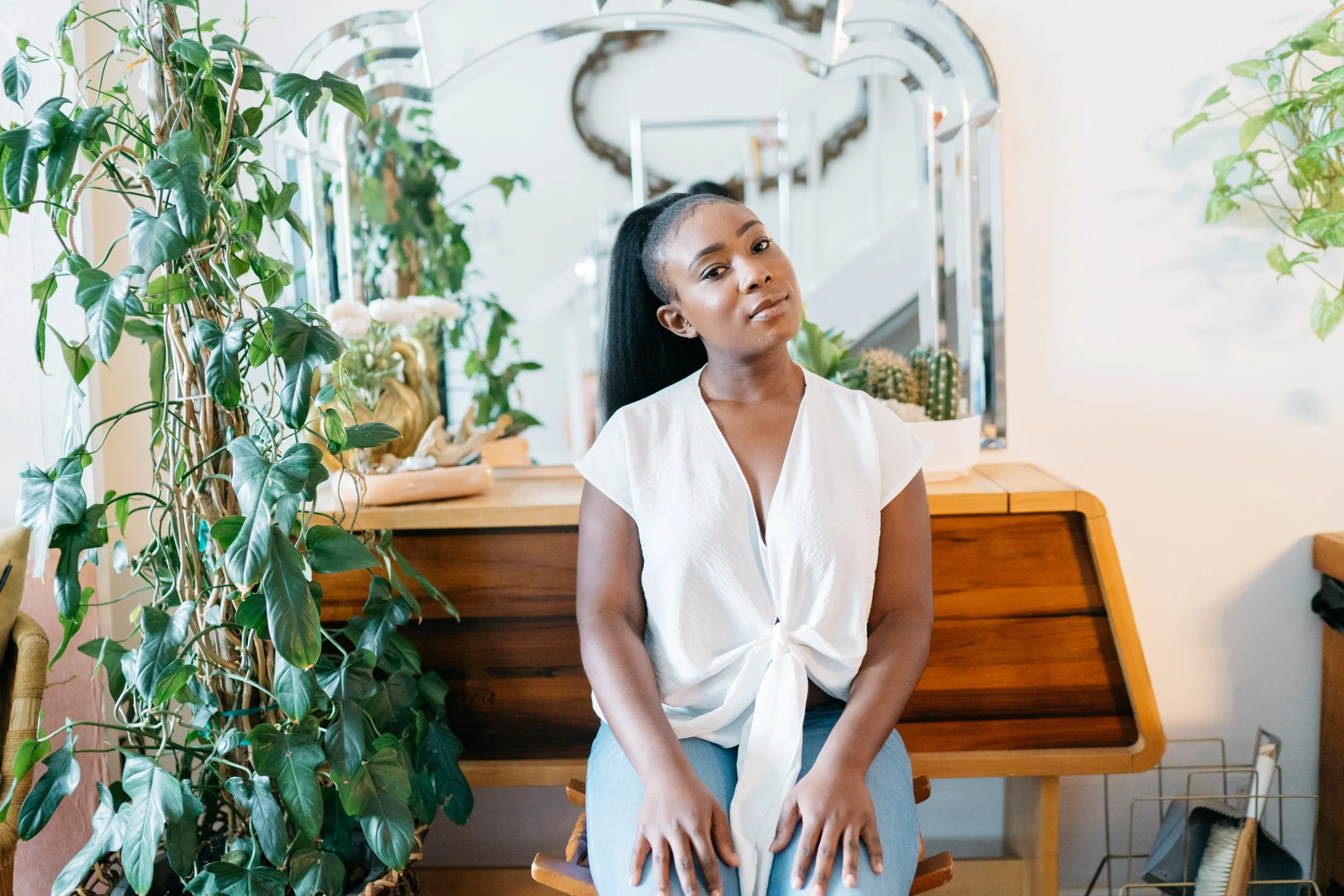 Image of Morgan Blackman, author of this post, sitting on a wooden stool infront of wooden desk with tall vineyard plant to the left