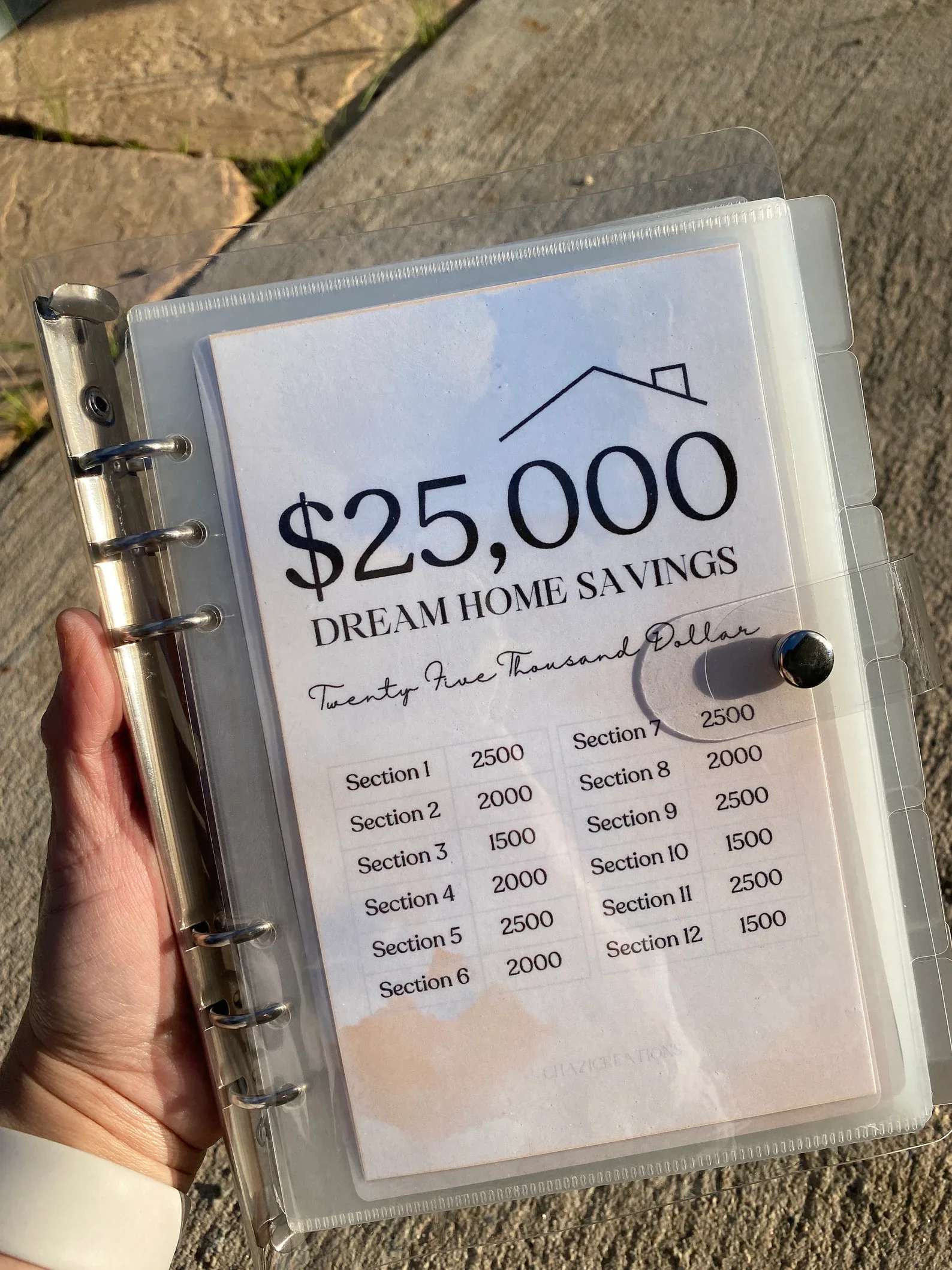 hand holding a dream home savings binder with calculation breakdwon on saving $25,000