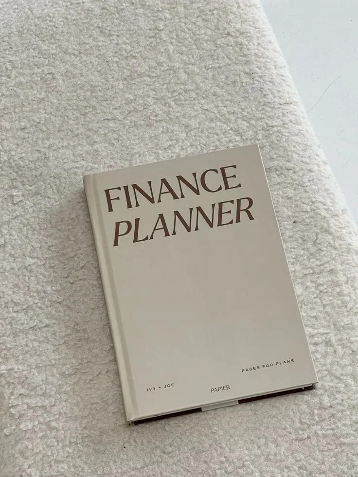 white book labelled finance planner in bold brown colored font sitting atop a wool table cloth