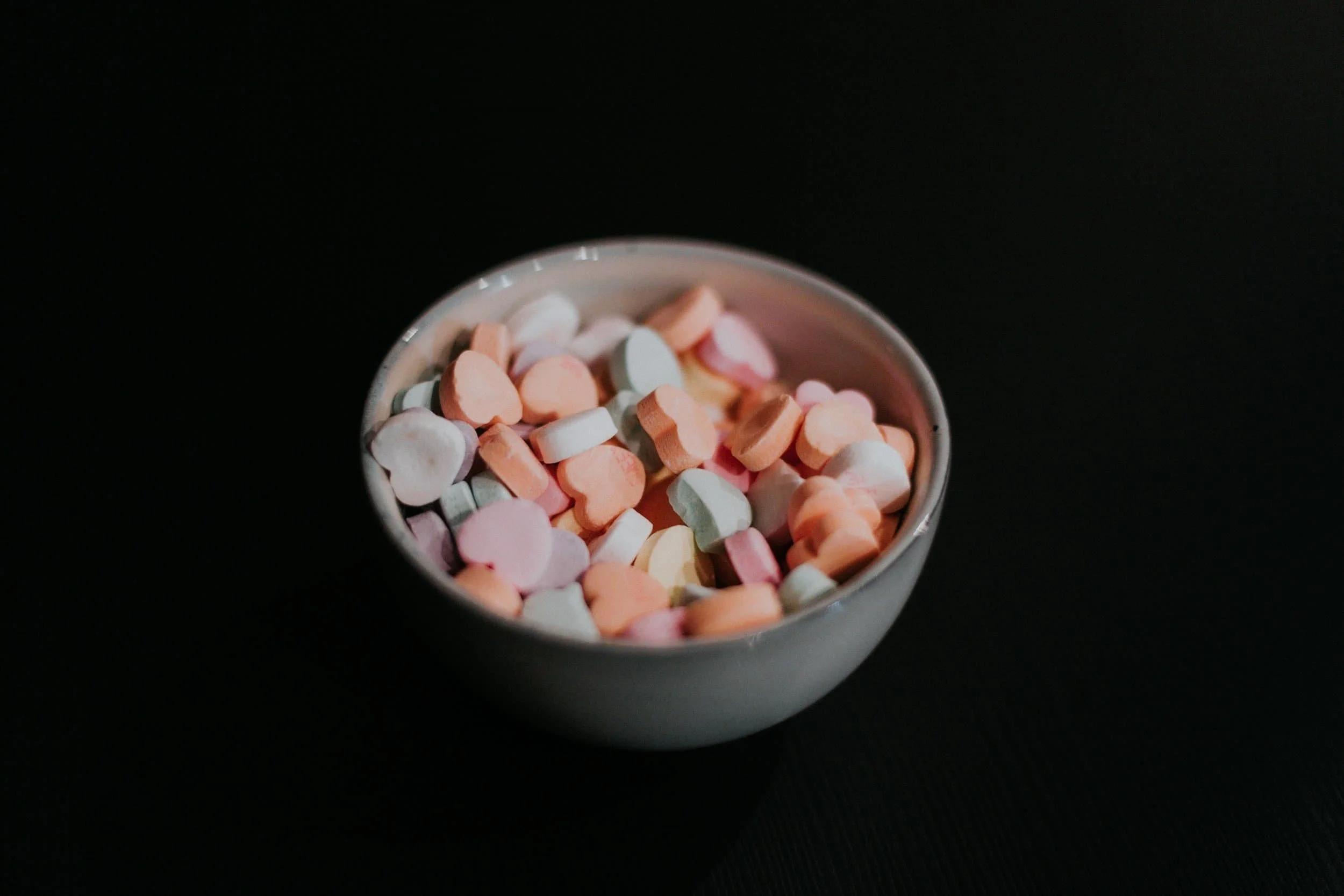 bowl of dry candied hearts in different colors amidst black backdrop