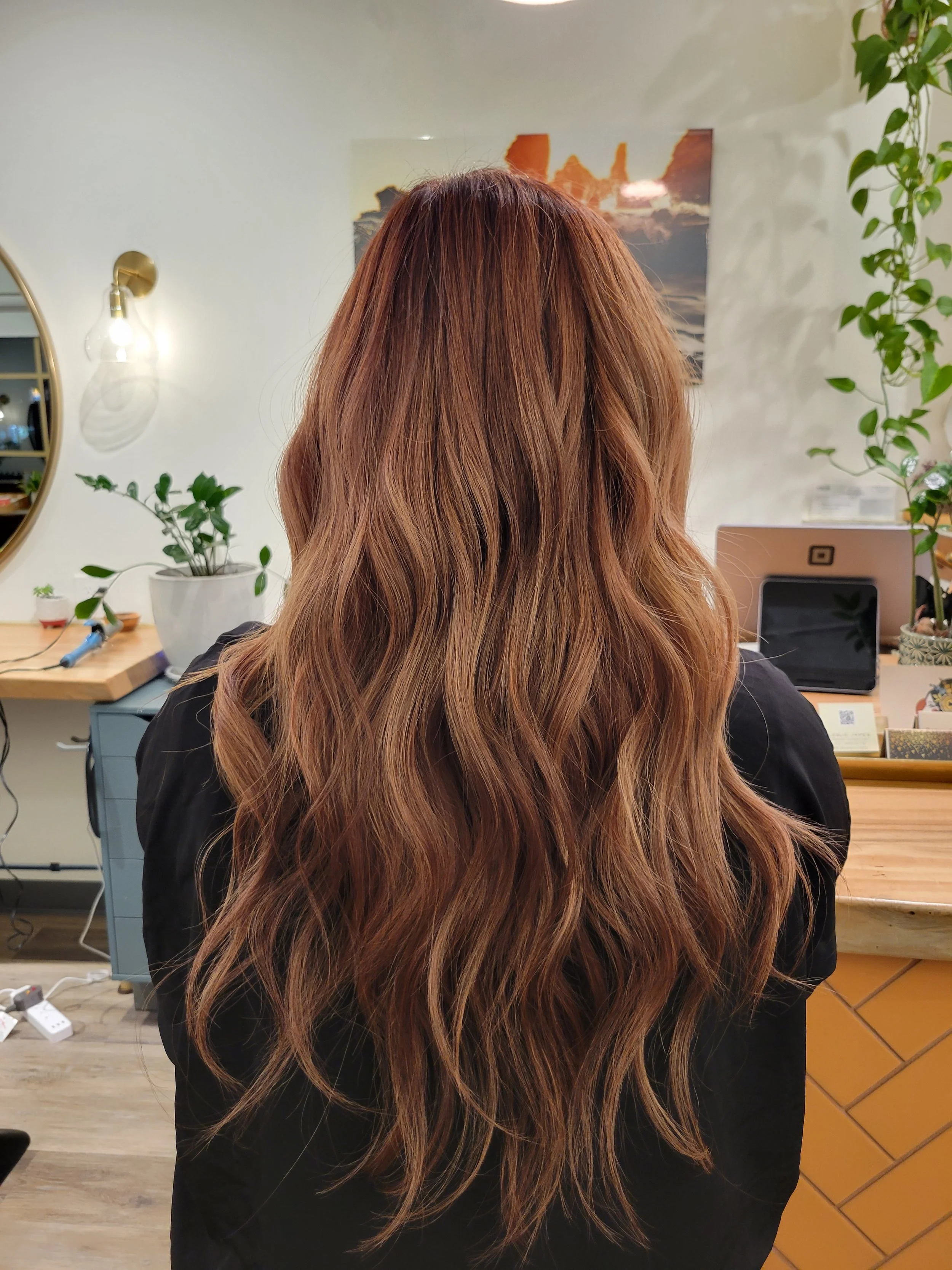 Back of a woman with long, wavy, auburn hair in a salon.