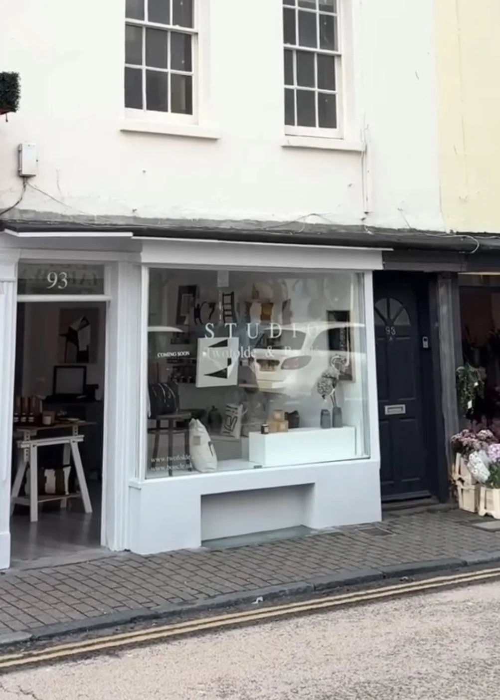 Facade of a storefront named 'STUDIO' with large display window, white exterior, and black door, located at 93.
