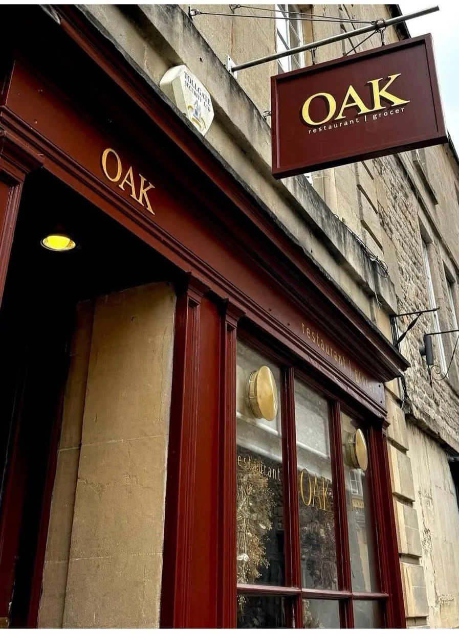 Exterior view of a restaurant called OAK with a hanging sign and red window frames, in a stone building.