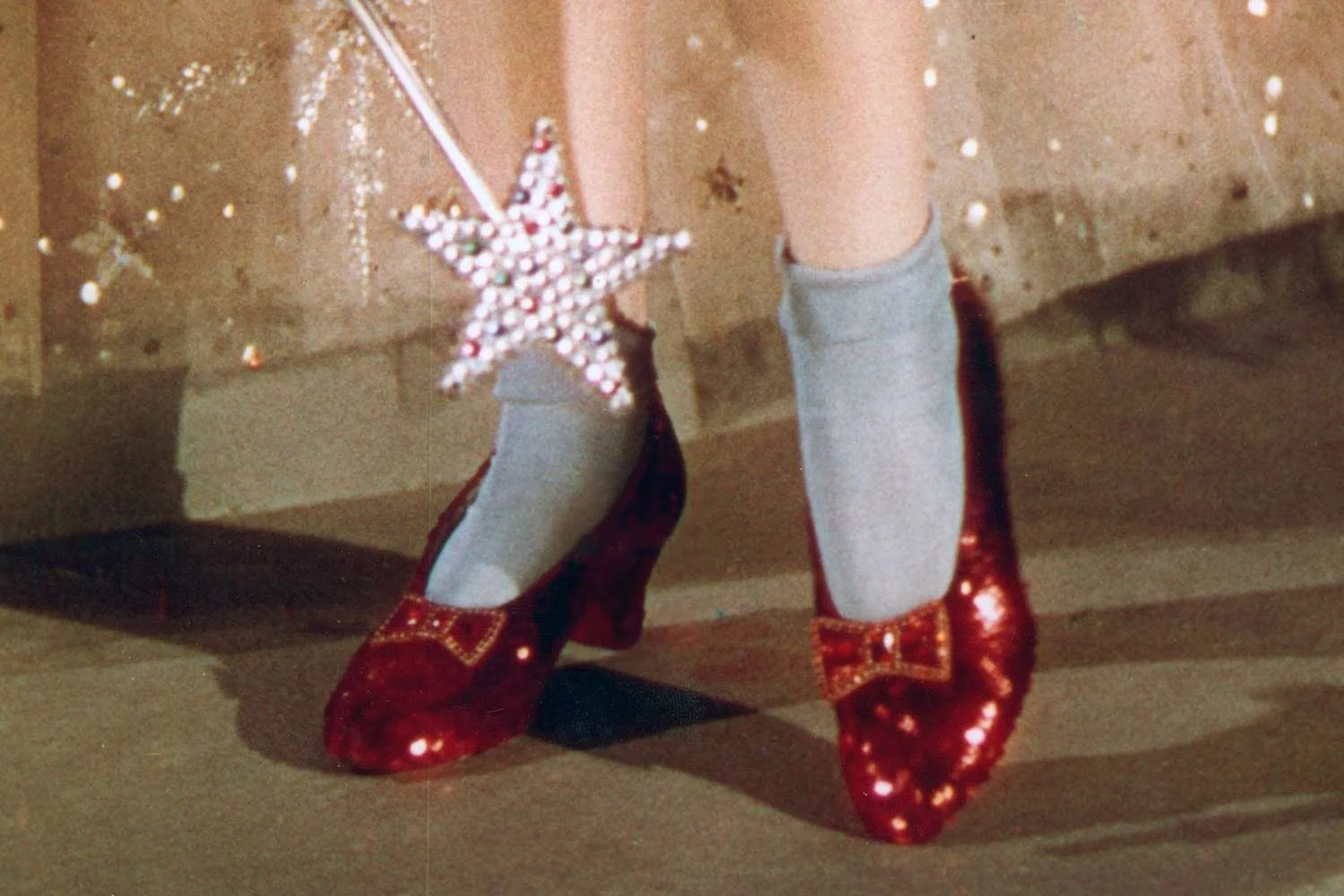 Dorothy clicking the heels of her shiny red shoes with light blue ankle socks as the good witch uses her star-shaped wand to help her return home.