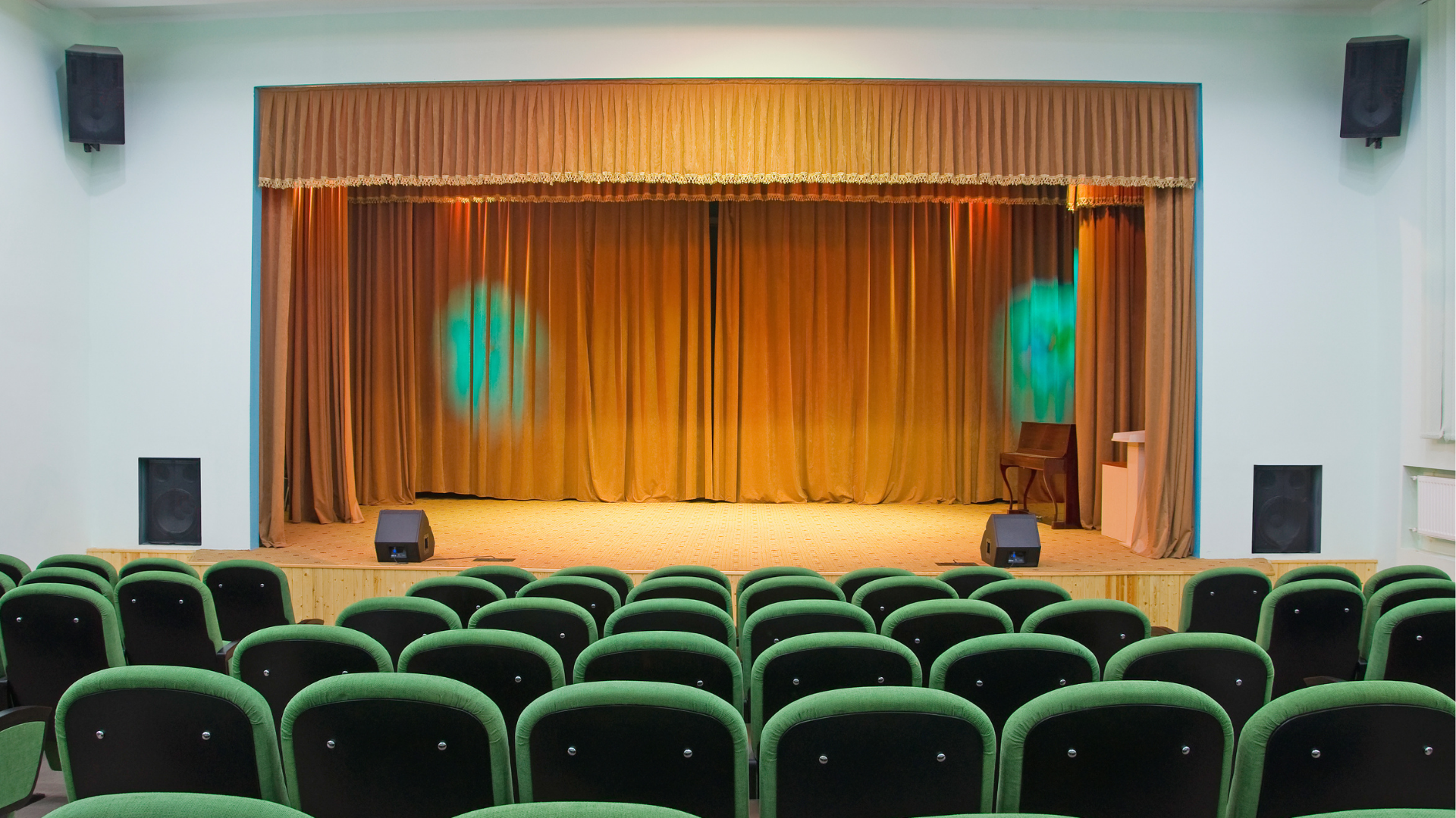small auditorium setting with a green seats in front of a stage
