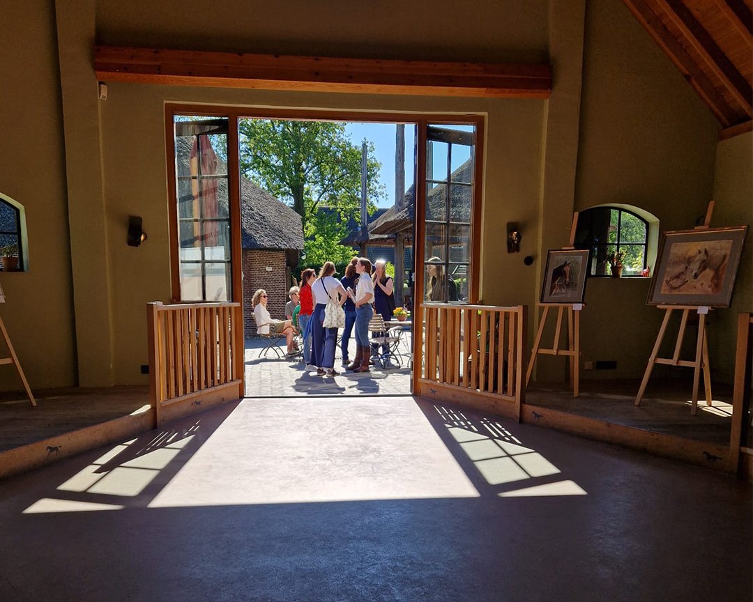 People inside an art gallery looking out through open doors at a group of people outside, with paintings on easels inside.