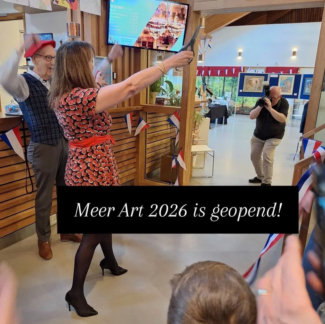 Two women, one older and one younger, celebrating at an art opening event with confetti and flags, while a photographer takes pictures in the background. Screen displaying art details is visible.