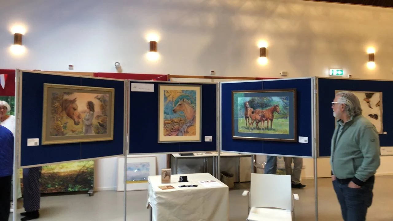 People viewing framed horse paintings at an art exhibition in an indoor gallery.