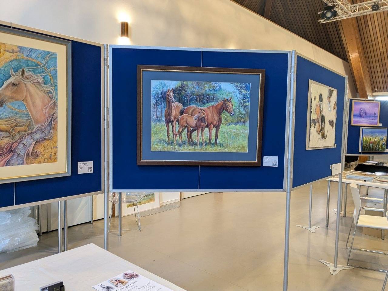An art gallery displaying paintings of horses, with a central painting showing a herd of brown horses in a grassy field and trees in the background.