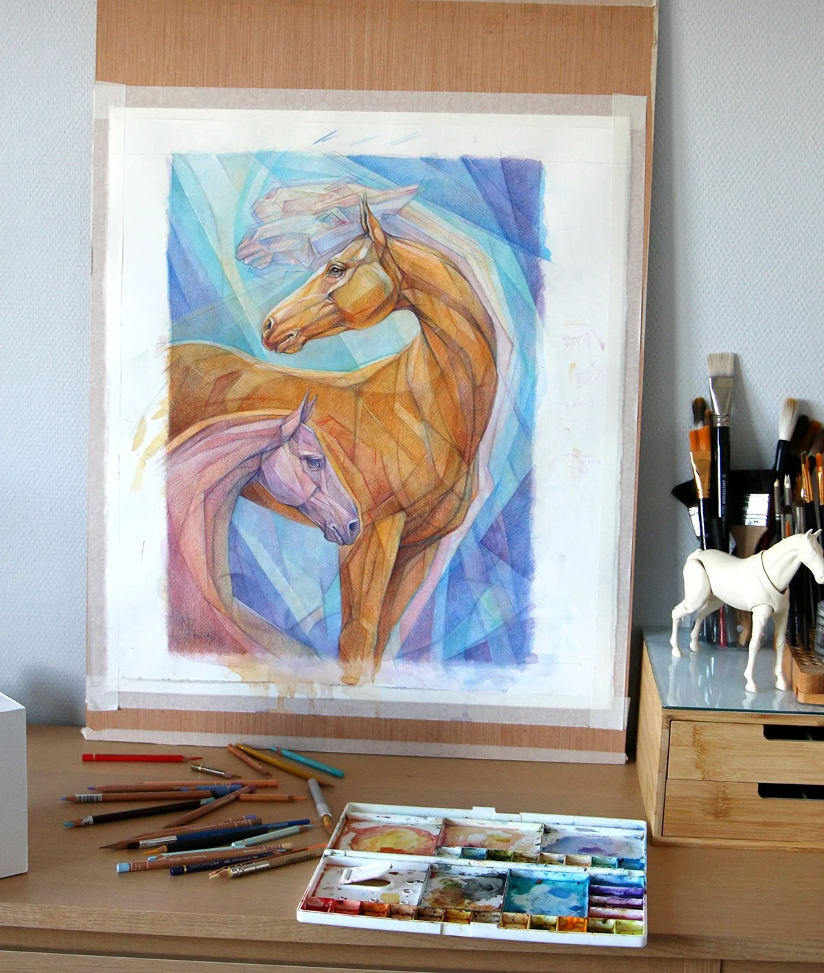Colorful painting of two horses in a geometric style, on an easel with paint supplies and brushes nearby.